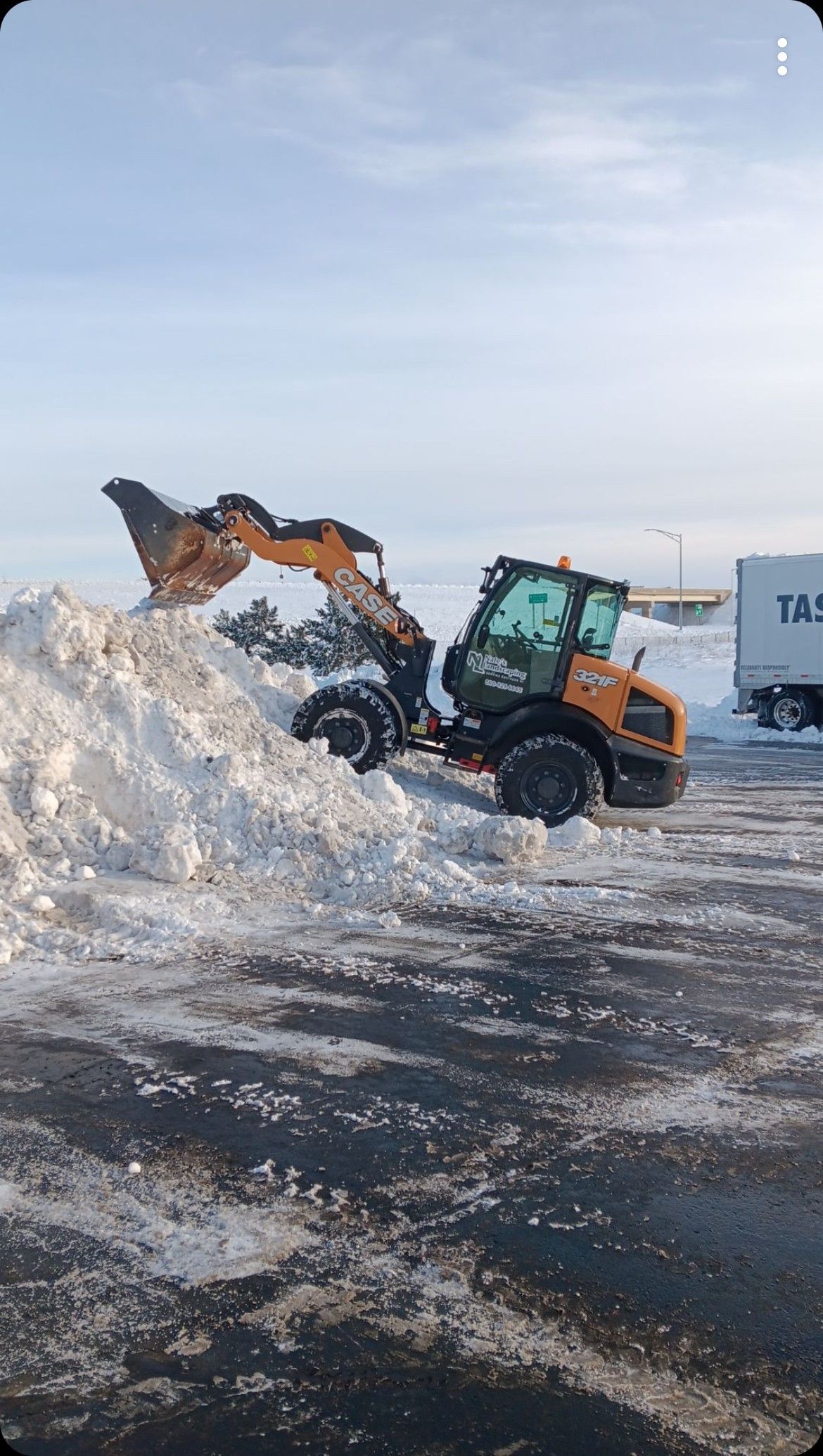 An orange snowplow scoops a pile of snow in a snow-covered parking lot.