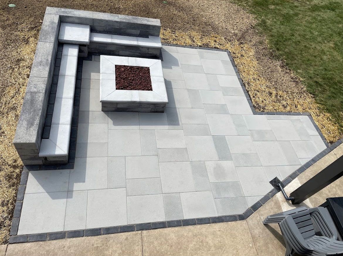 Patio with gray pavers, fire pit, built-in seating, black border, and surrounding gravel.