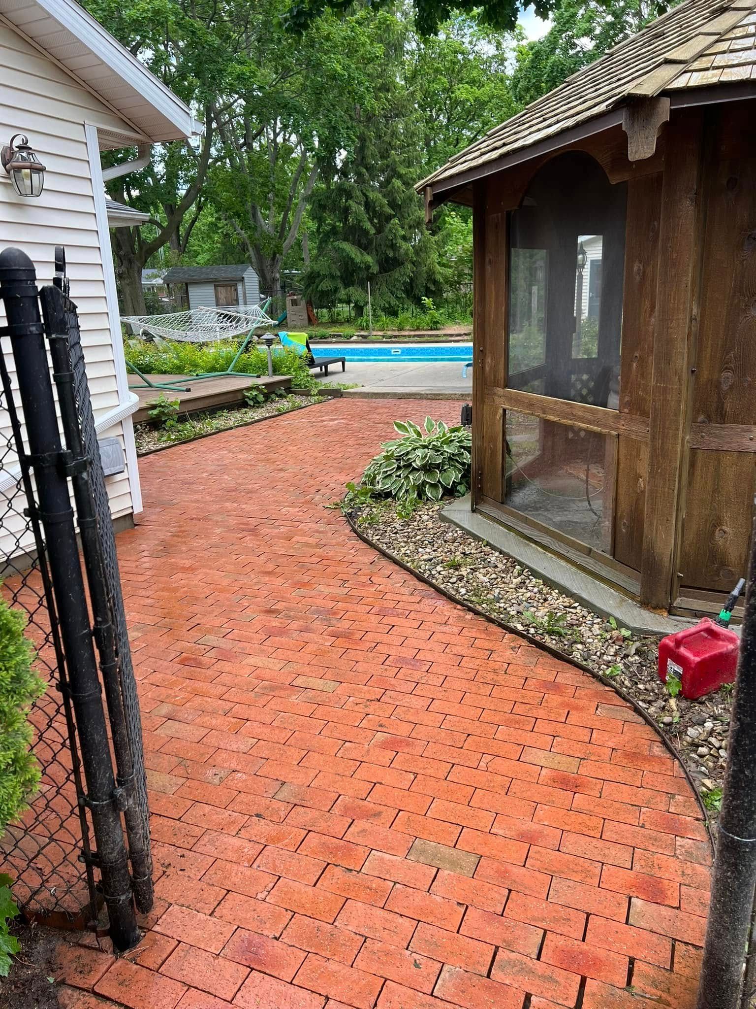 Brick pathway leading to a pool and gazebo, next to a white building.