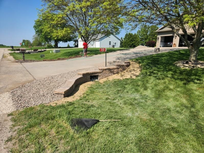 A residential driveway with a drainage ditch filled with gravel and a mailbox in the middle.