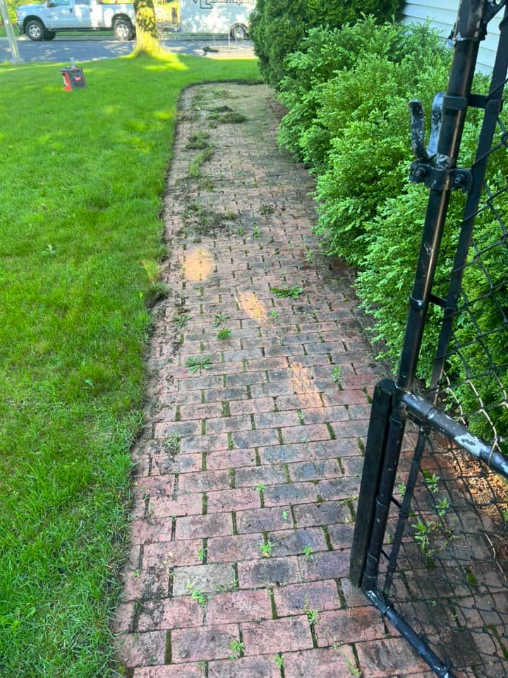 Brick pathway with green grass and bushes, leading to a black metal gate.