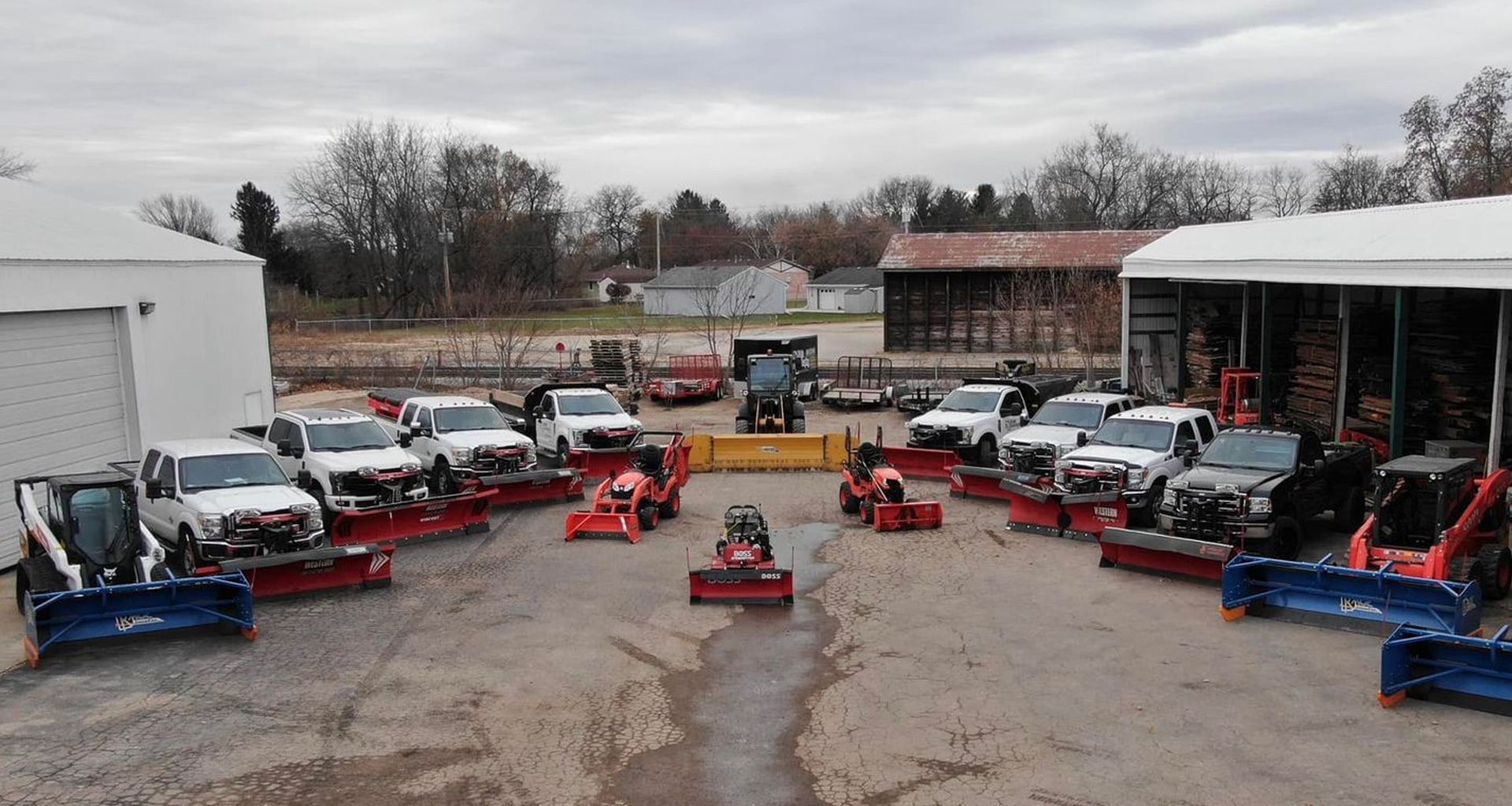 snowplows and trucks arranged in a semi-circle, in front of buildings on a cloudy day