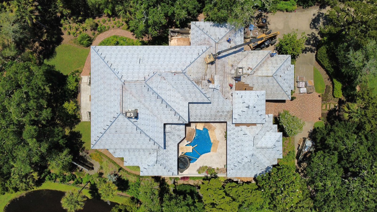 Aerial view of a large house with a blue pool, surrounded by trees and a walkway.