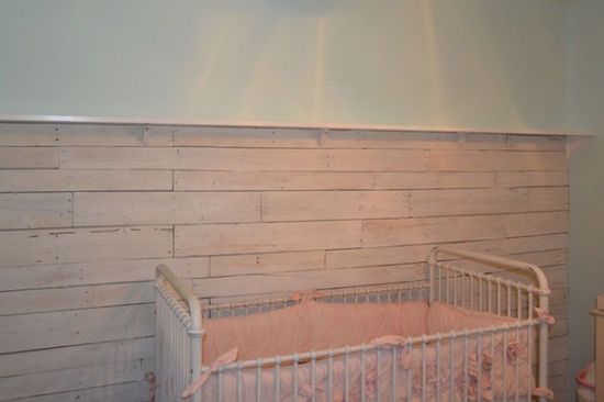 A baby crib in a nursery with a wooden wall behind it.