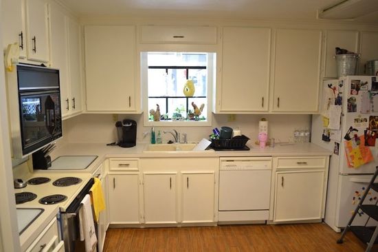 A kitchen with white cabinets , a stove , a dishwasher , and a window.