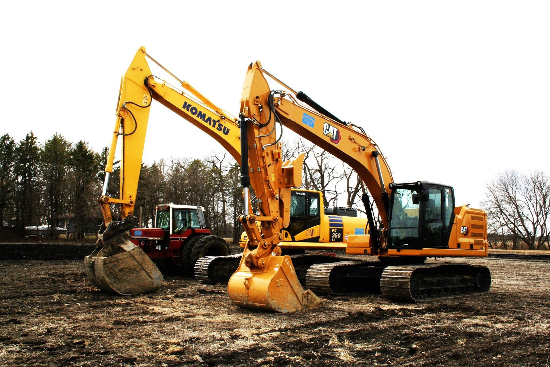 A yellow excavator is sitting next to a red tractor in a dirt field