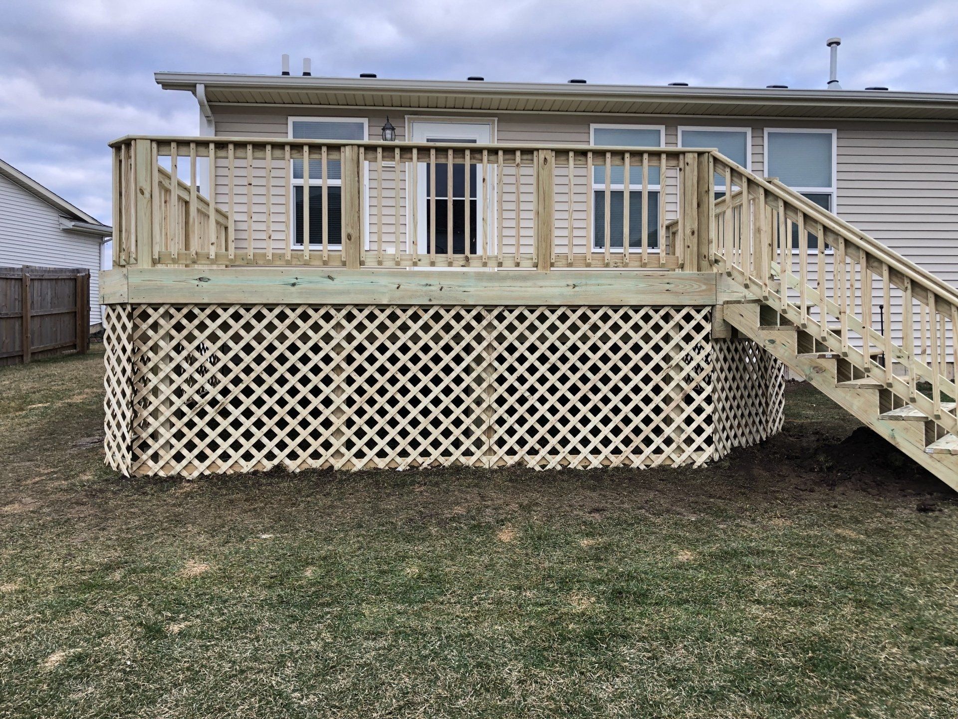 A wooden deck with stairs leading up to it is in the backyard of a house.