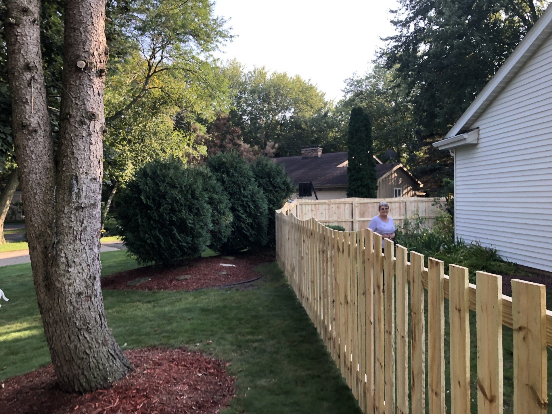 A wooden fence surrounds a lush green yard in front of a house.