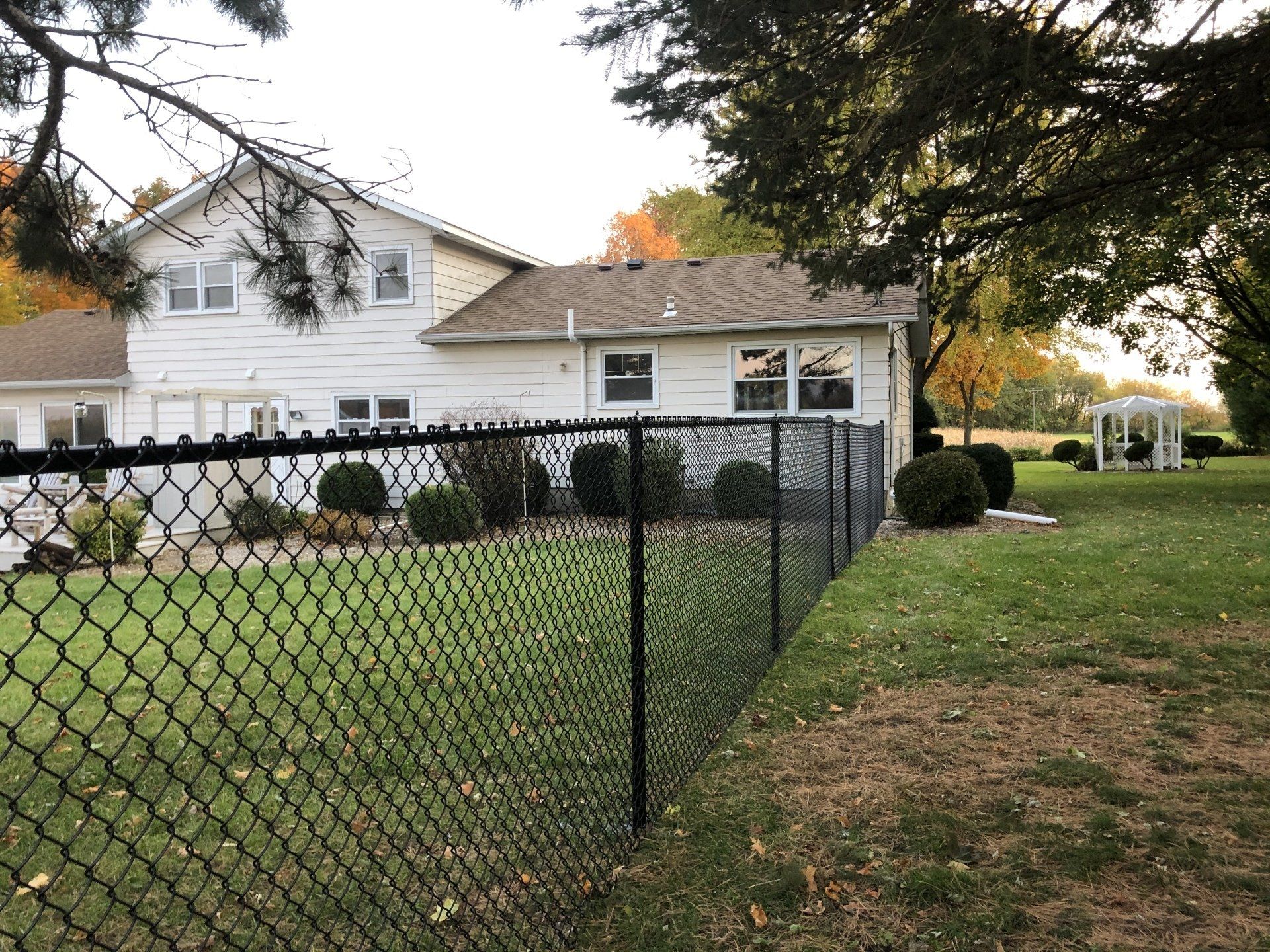 A chain link fence surrounds a large yard in front of a house.