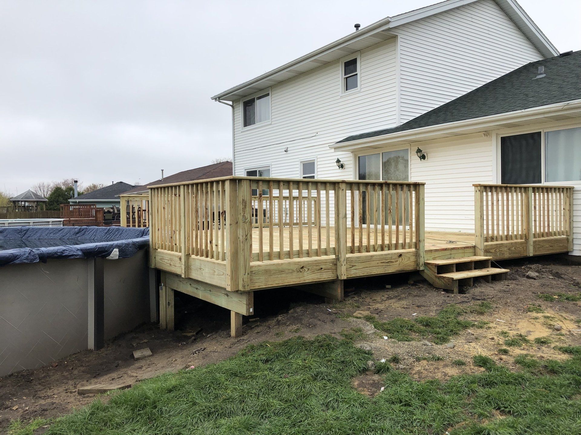 A wooden deck is in the backyard of a house next to a pool.