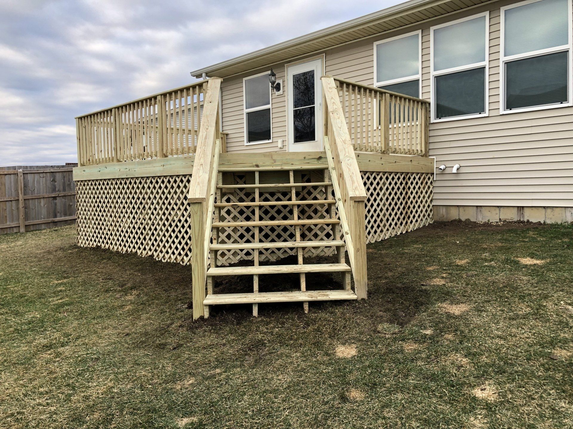 A wooden deck with stairs leading up to it is in front of a house.