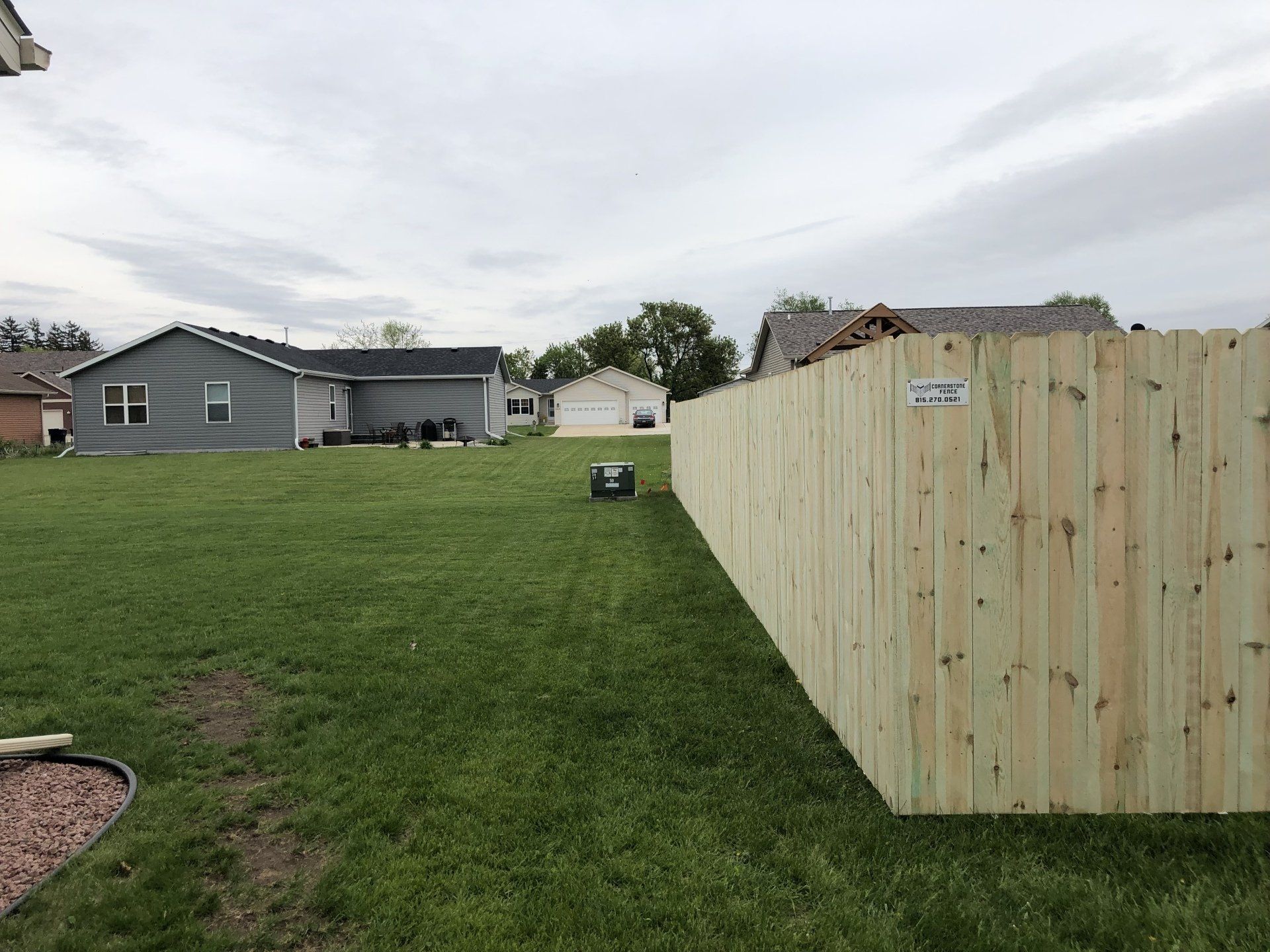 A wooden fence surrounds a lush green yard with a house in the background.
