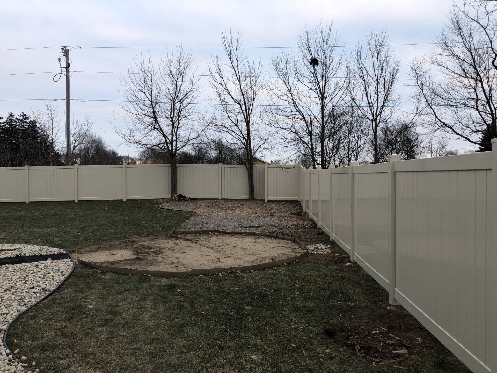 A white fence surrounds a grassy yard with trees in the background.