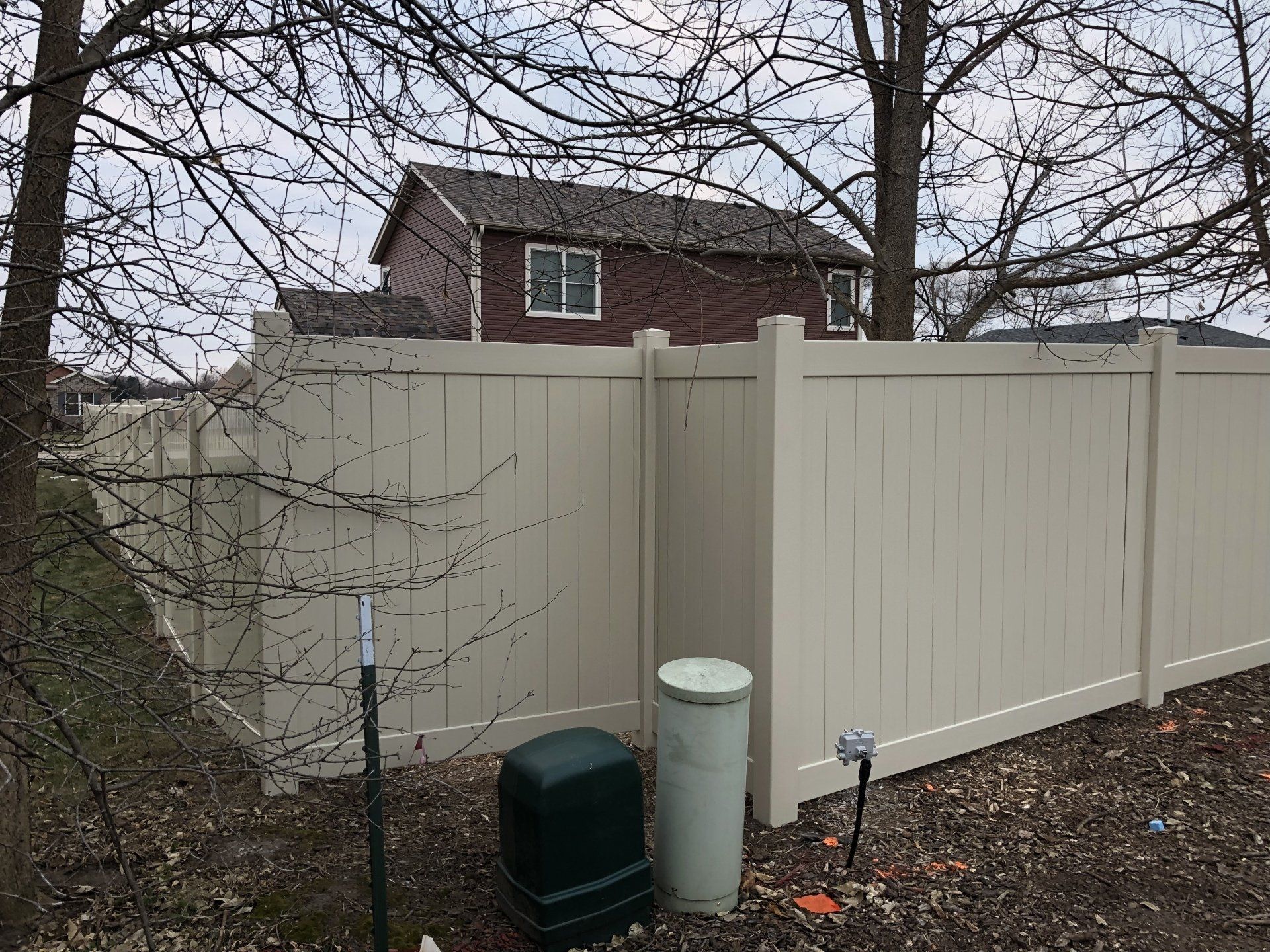 A white fence with a water heater and a house in the background.