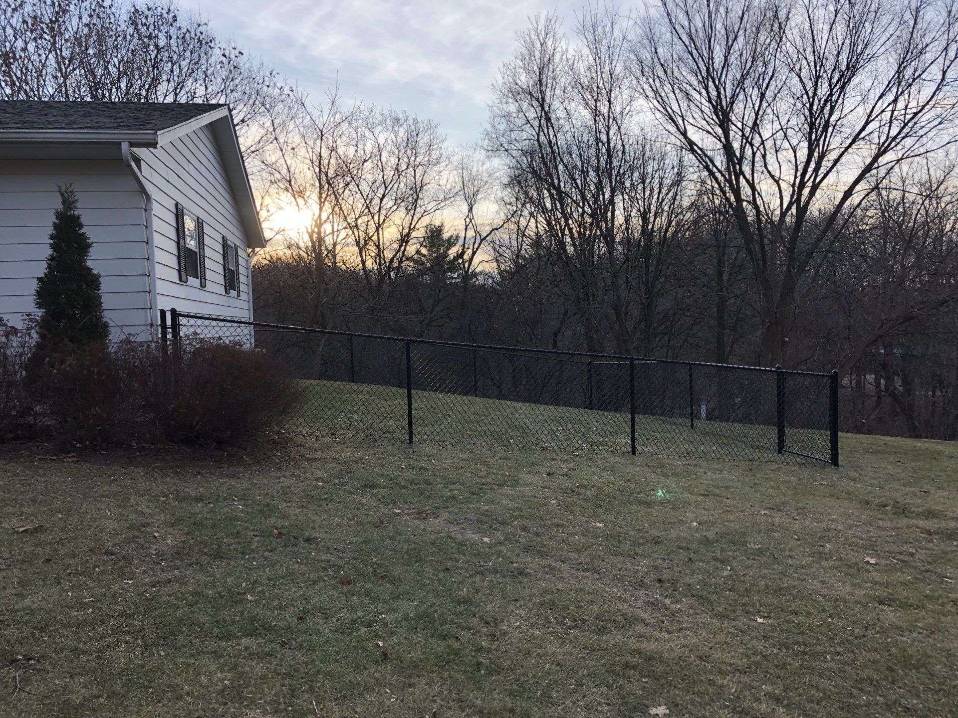 A white house is sitting on top of a grassy hill next to a chain link fence.