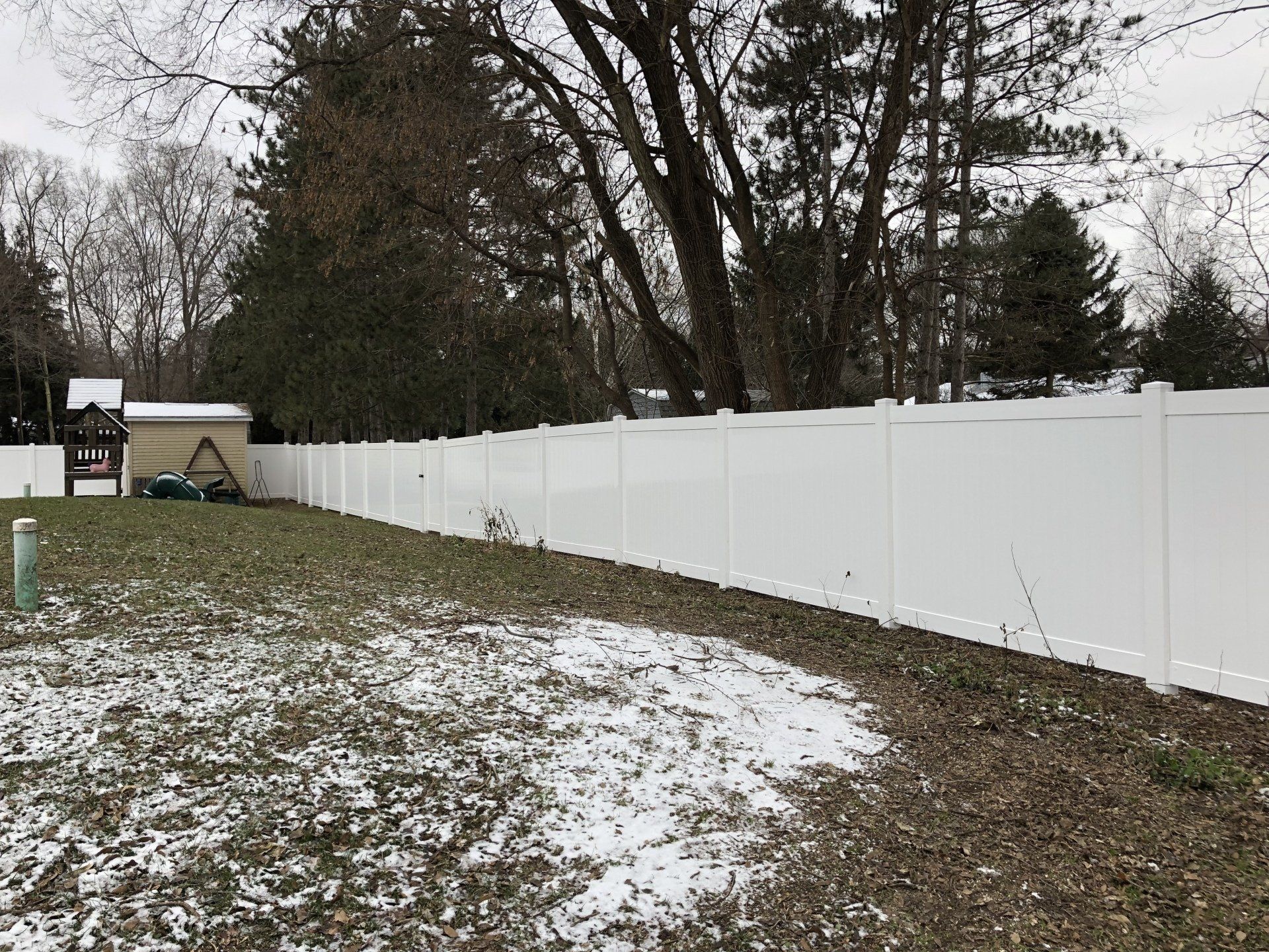 A white fence surrounds a snowy yard with trees in the background.