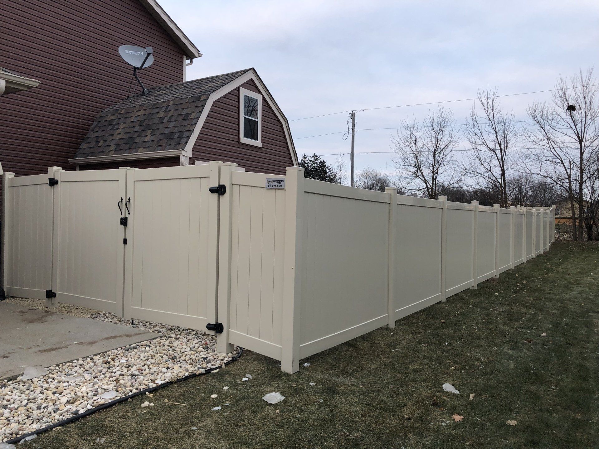 A white fence is surrounding a house with a barn in the background.