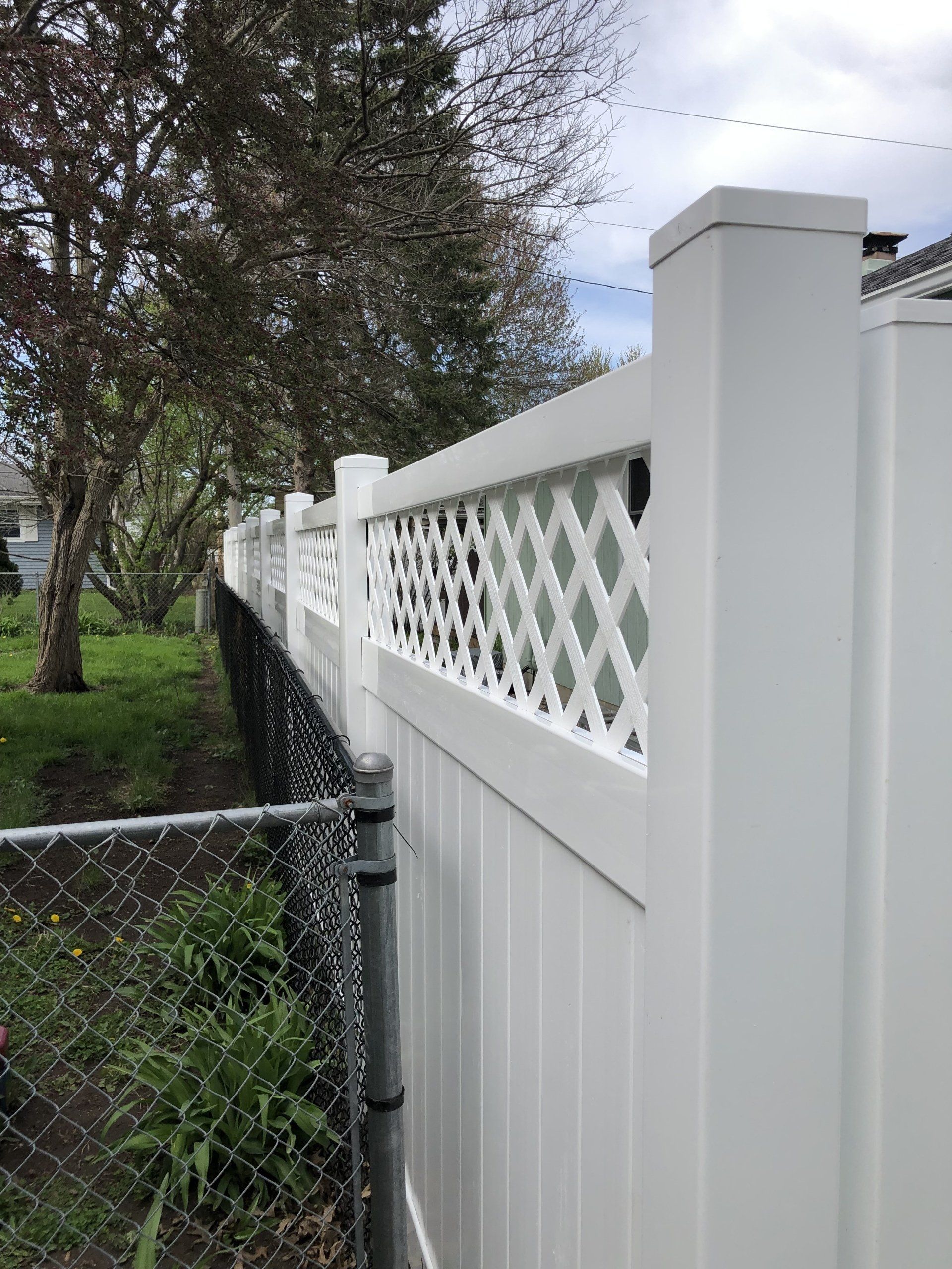 A white vinyl fence with a lattice design is next to a chain link fence.
