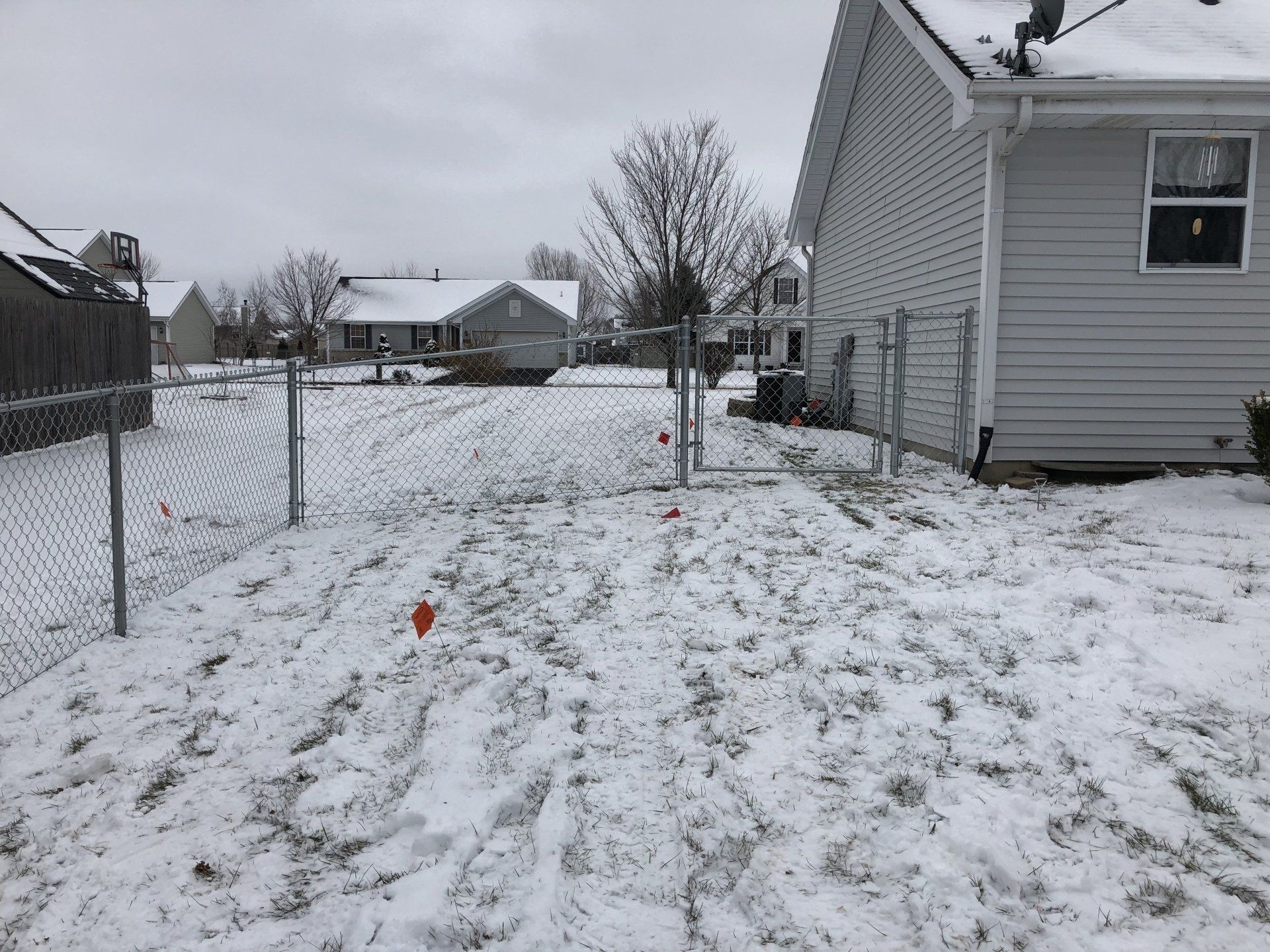 A snowy yard with a chain link fence and a house in the background.