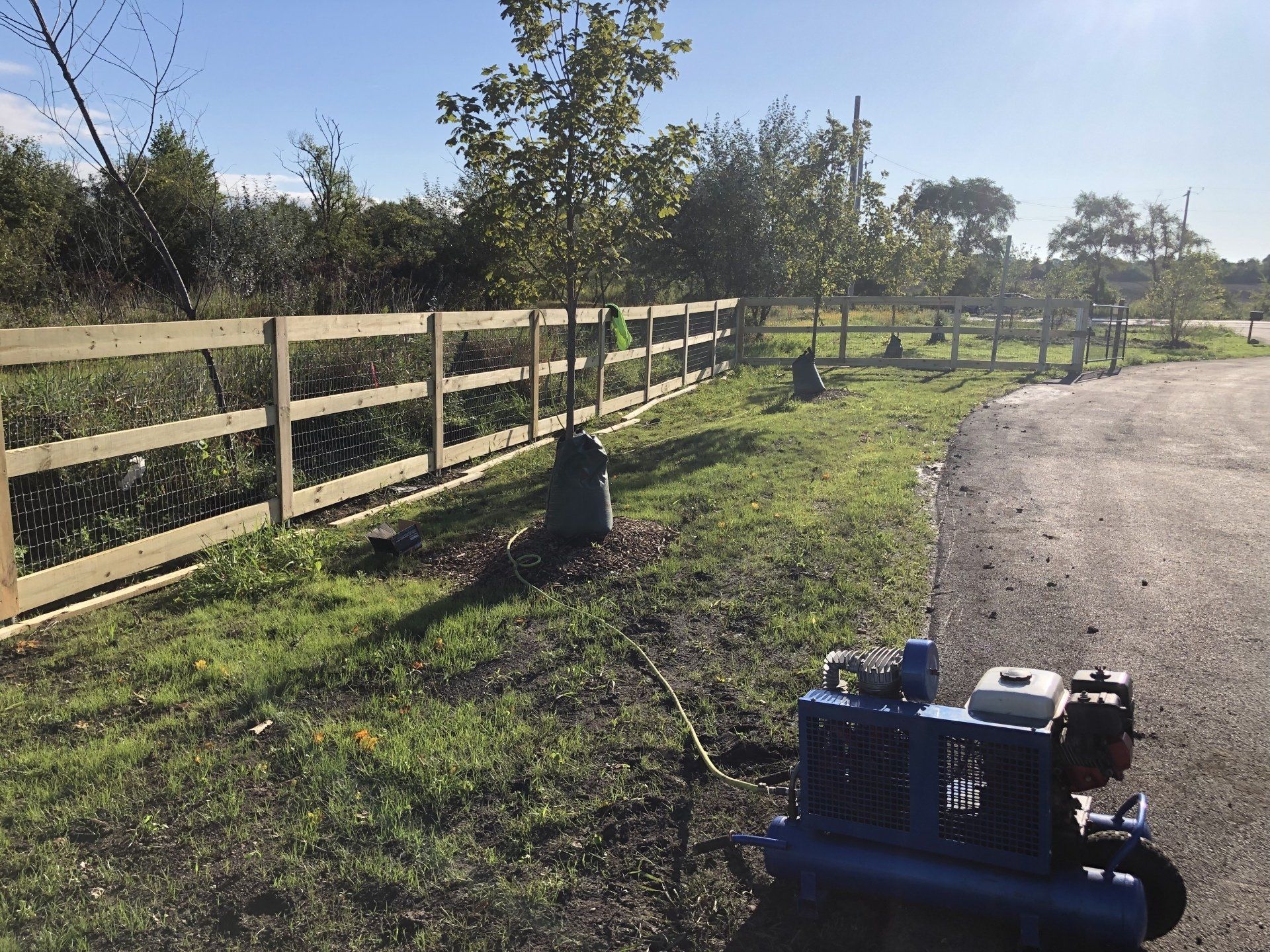 A blue air compressor is sitting in the grass next to a wooden fence.