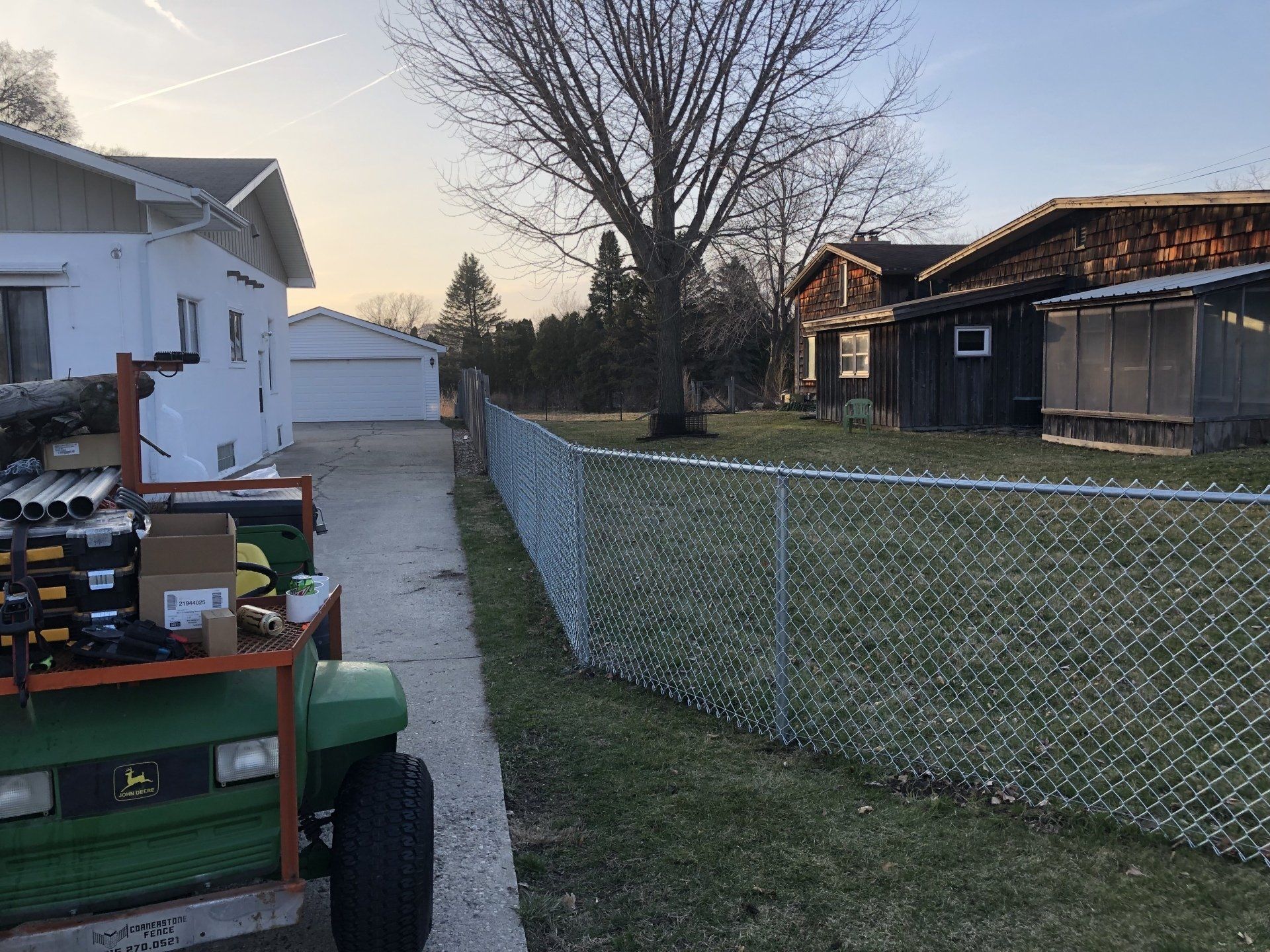 A green golf cart is parked on the side of the road next to a chain link fence.