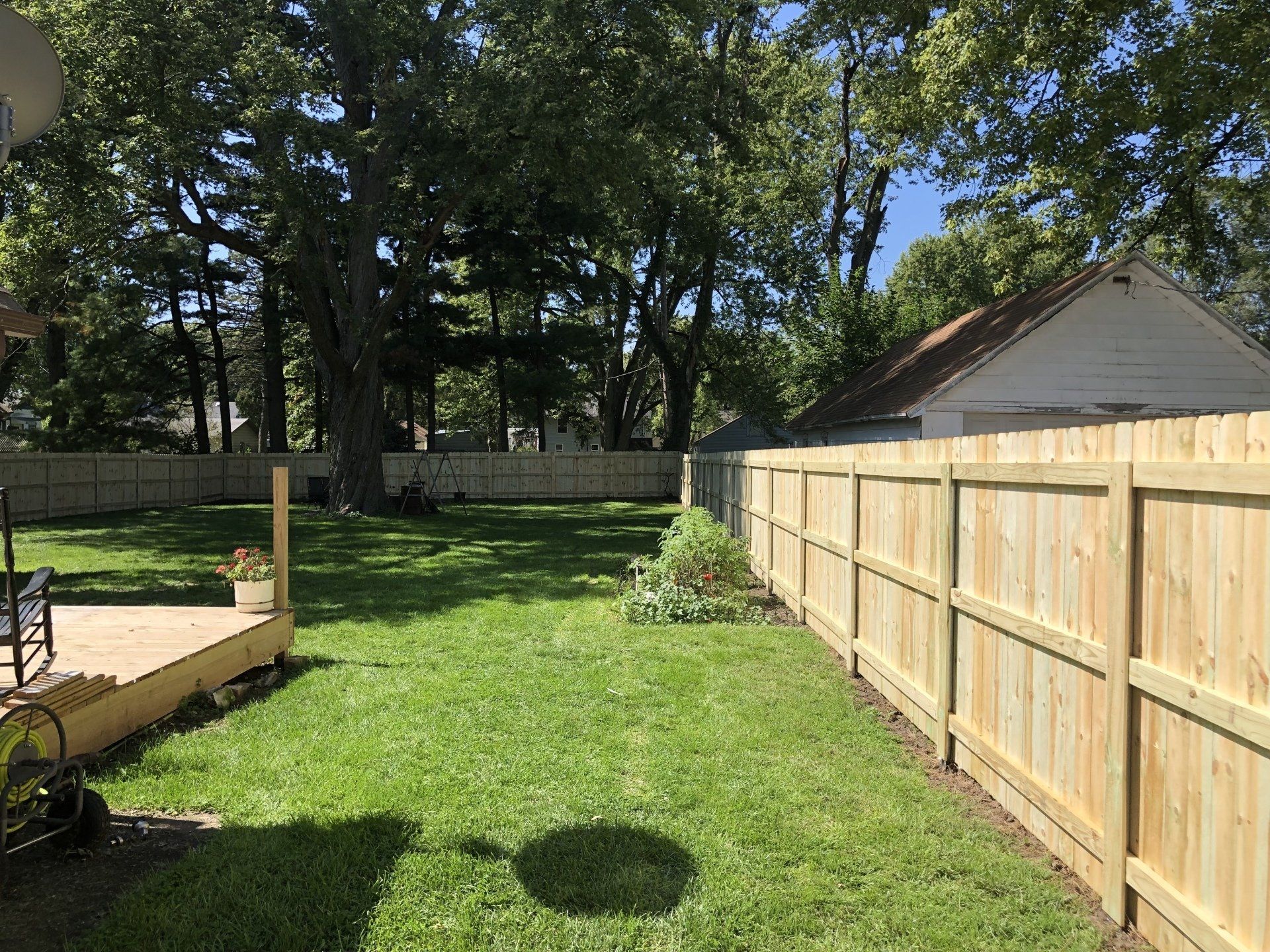 A wooden fence surrounds a lush green lawn in a backyard.
