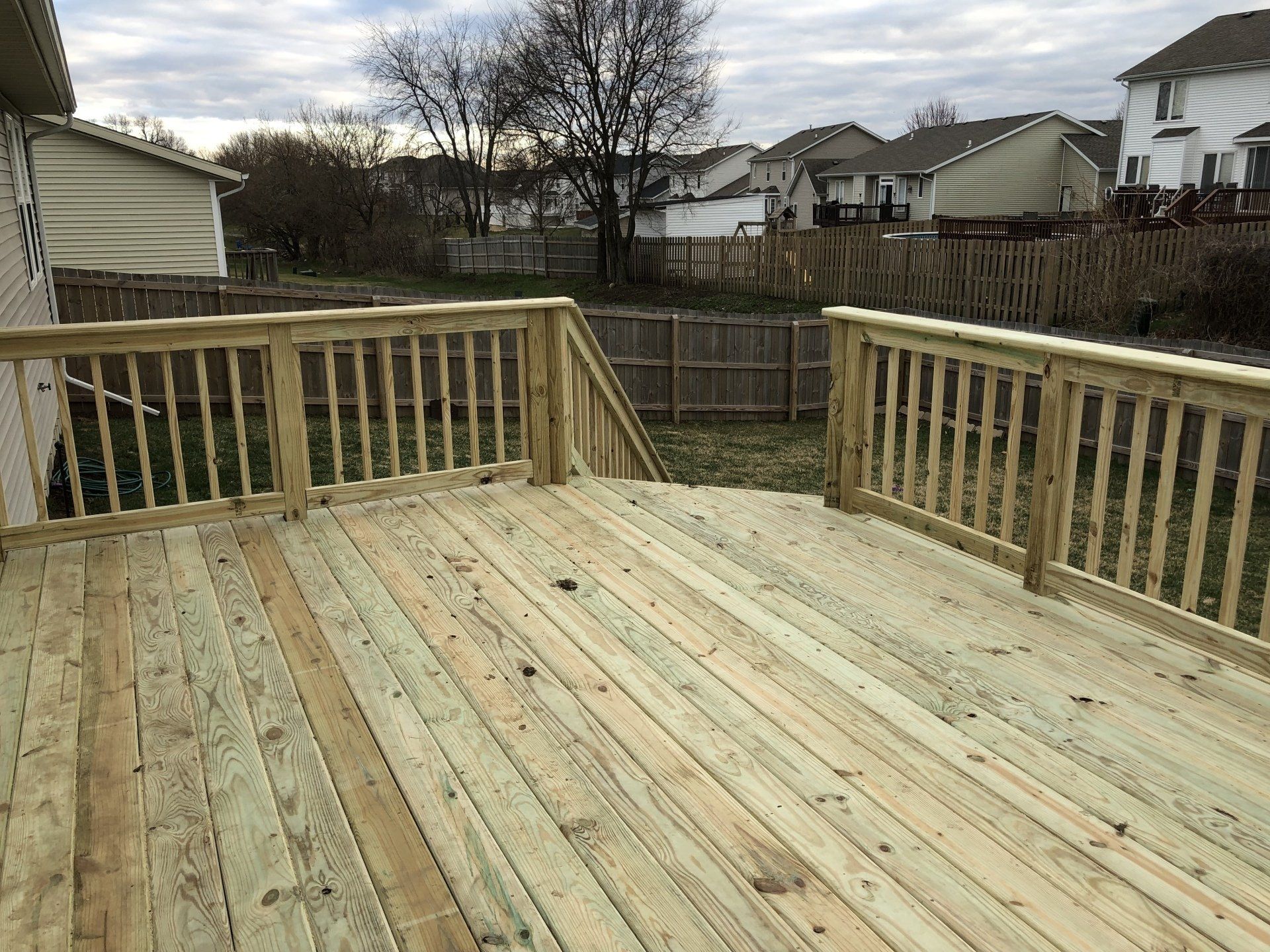 A large wooden deck with stairs leading up to it is in the backyard of a house.