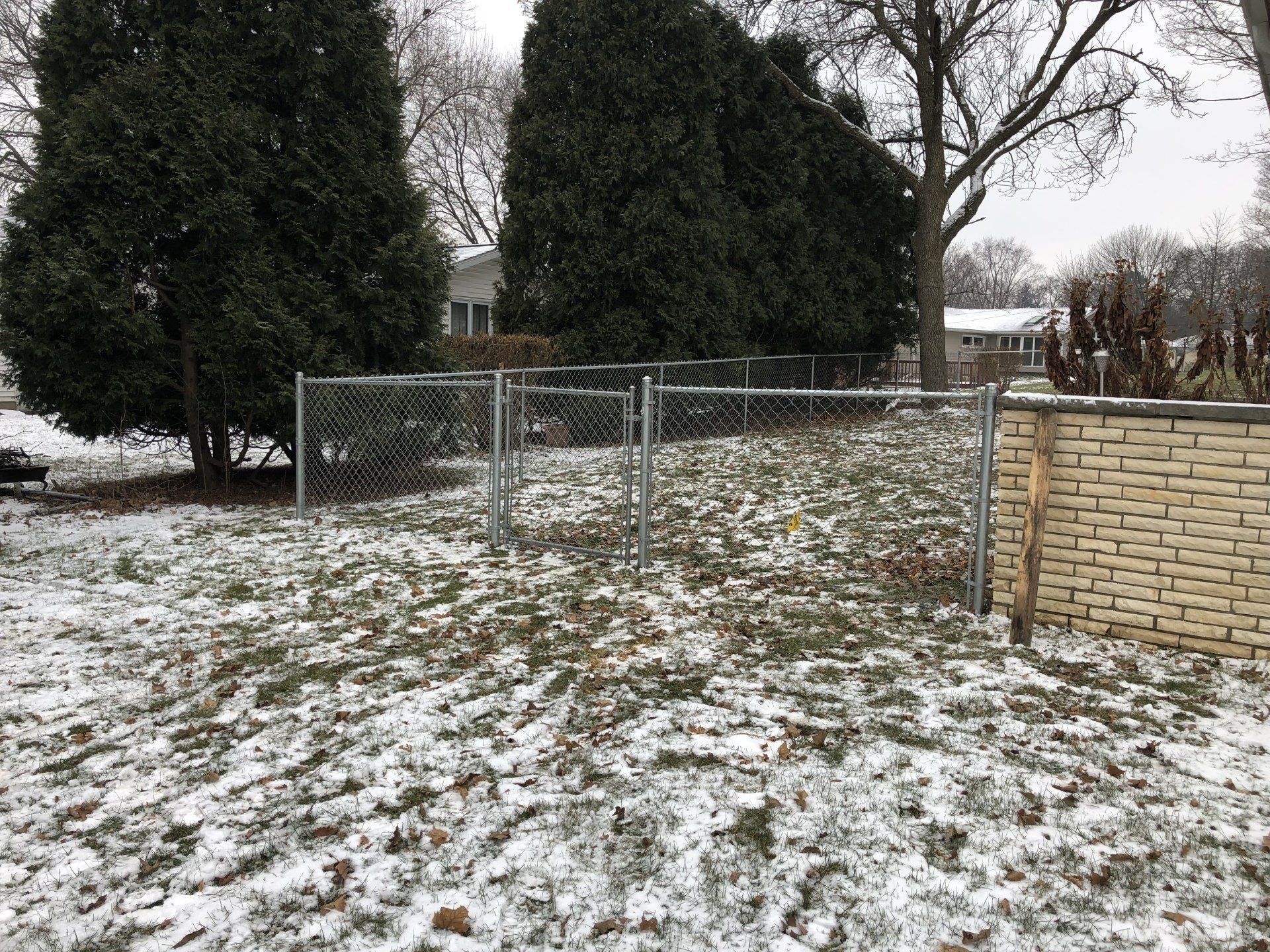 A snowy yard with a chain link fence and a brick wall.