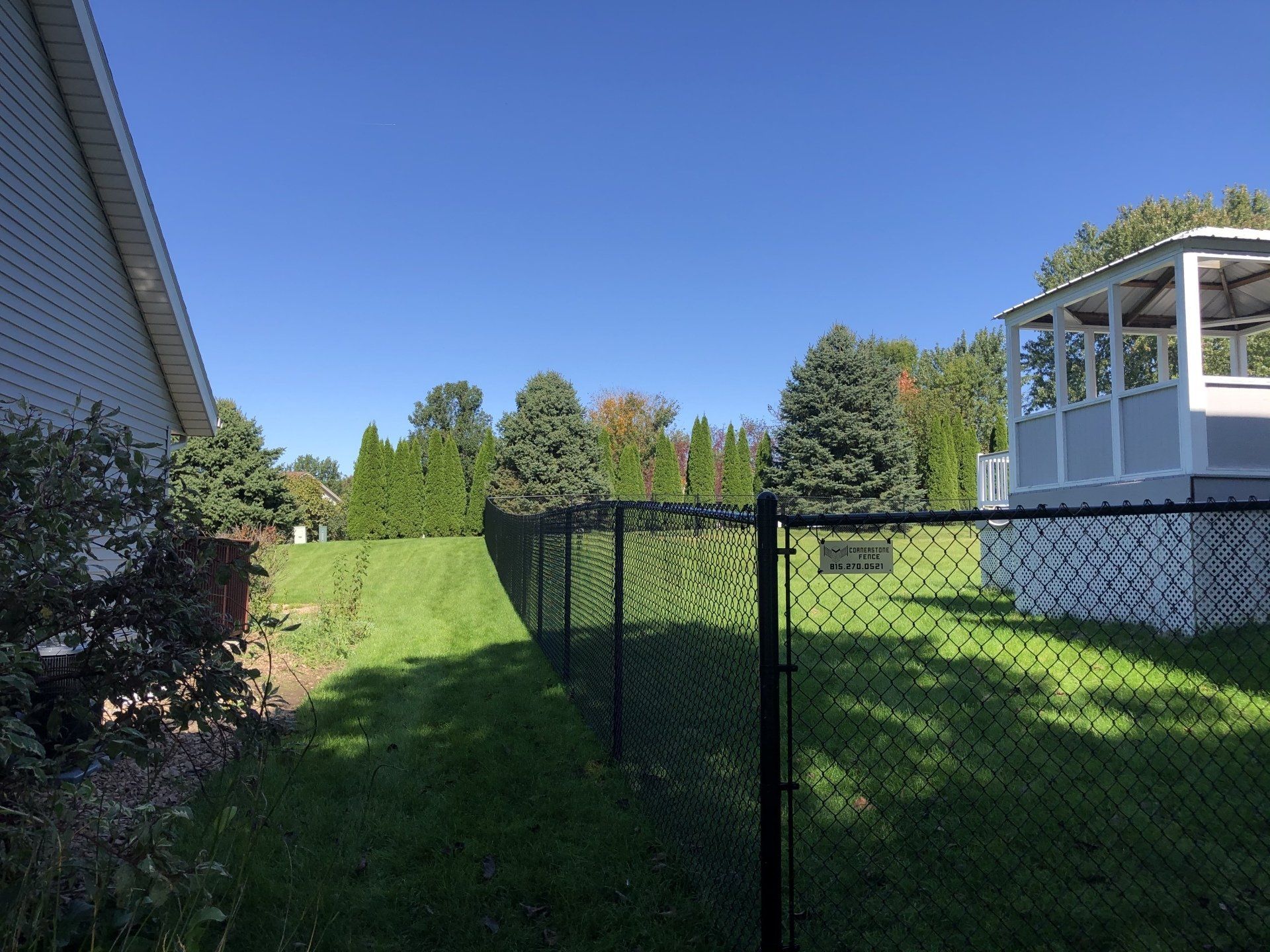 A chain link fence surrounds a lush green yard with a gazebo in the background.