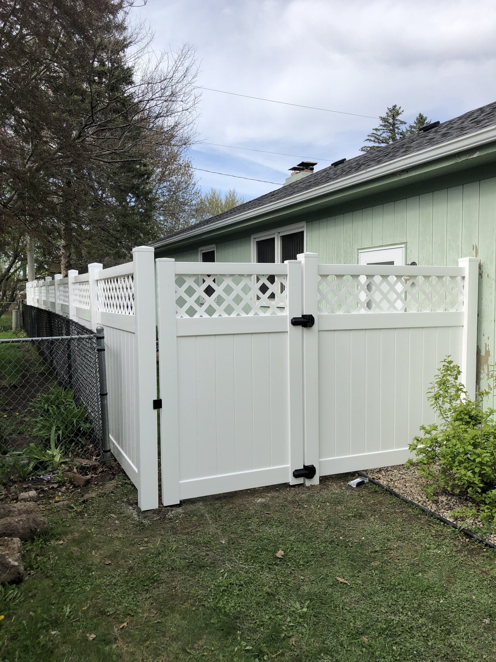 A white fence with a gate is in front of a green house.
