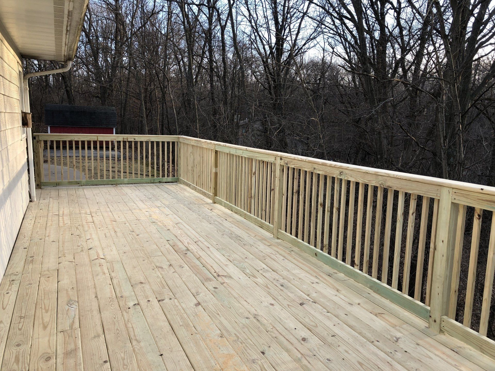 A large wooden deck with a railing and trees in the background.