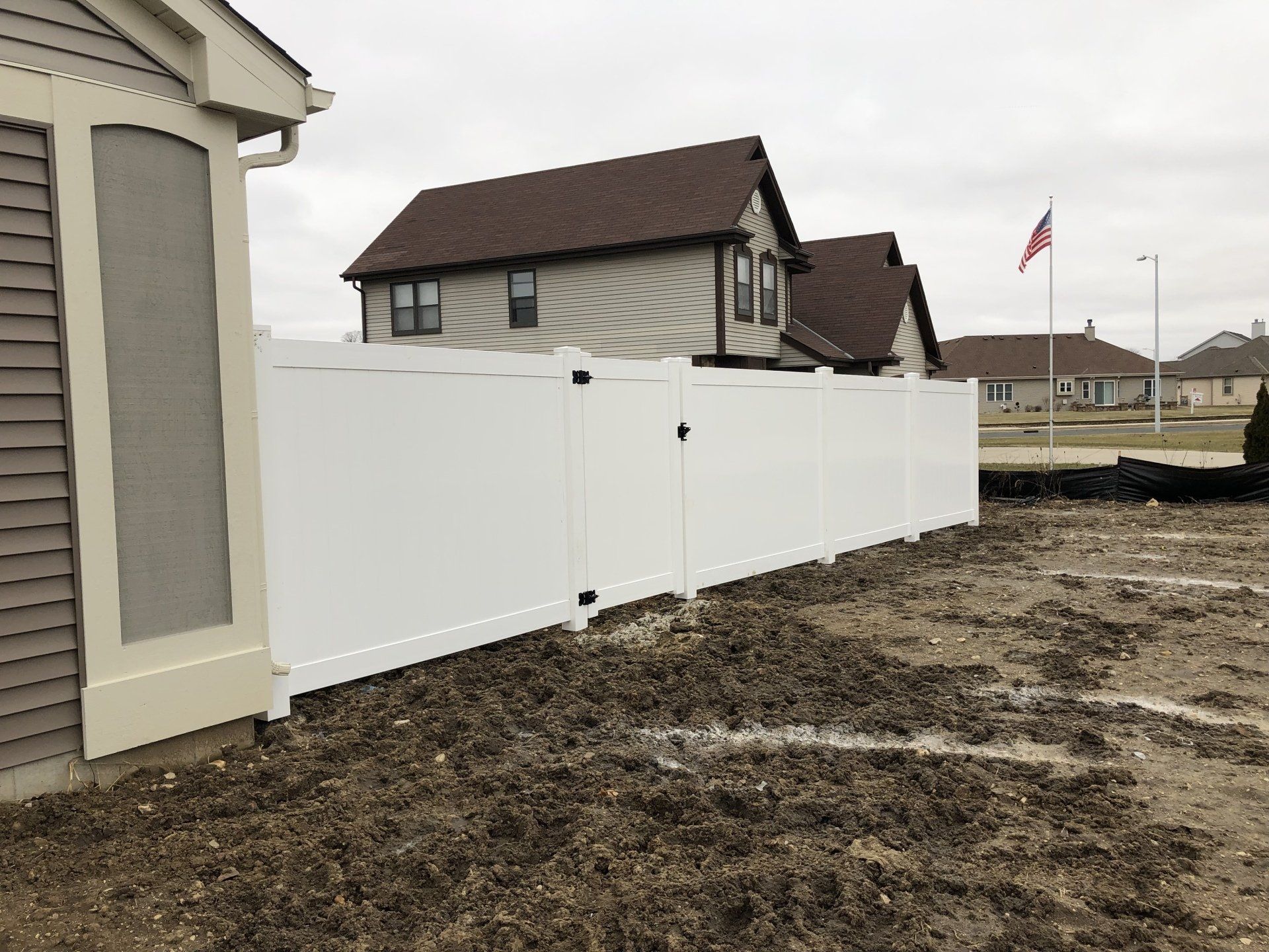 A white fence is surrounding a dirt field in front of a house.