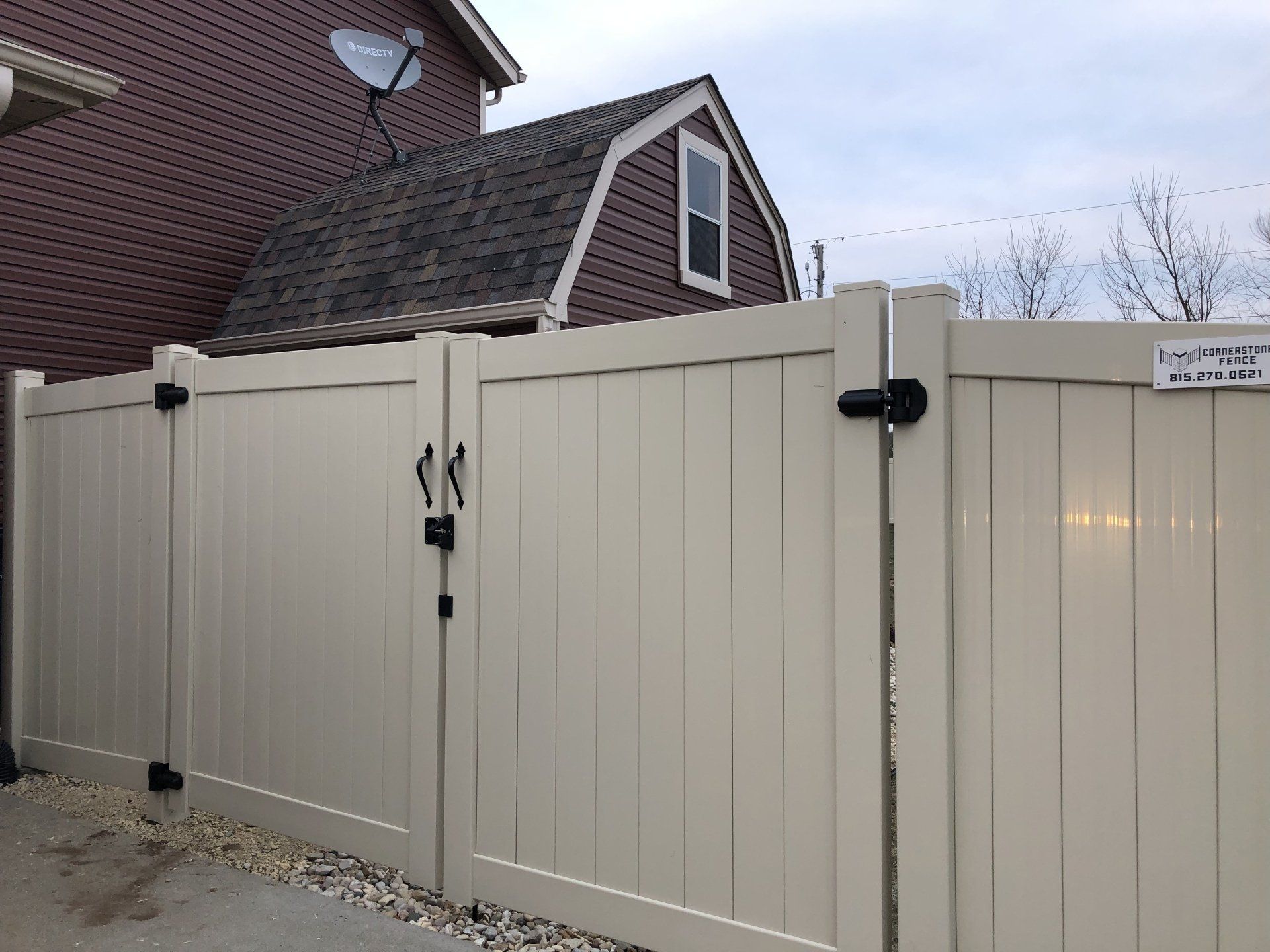A white fence with a gate in front of a brown house.
