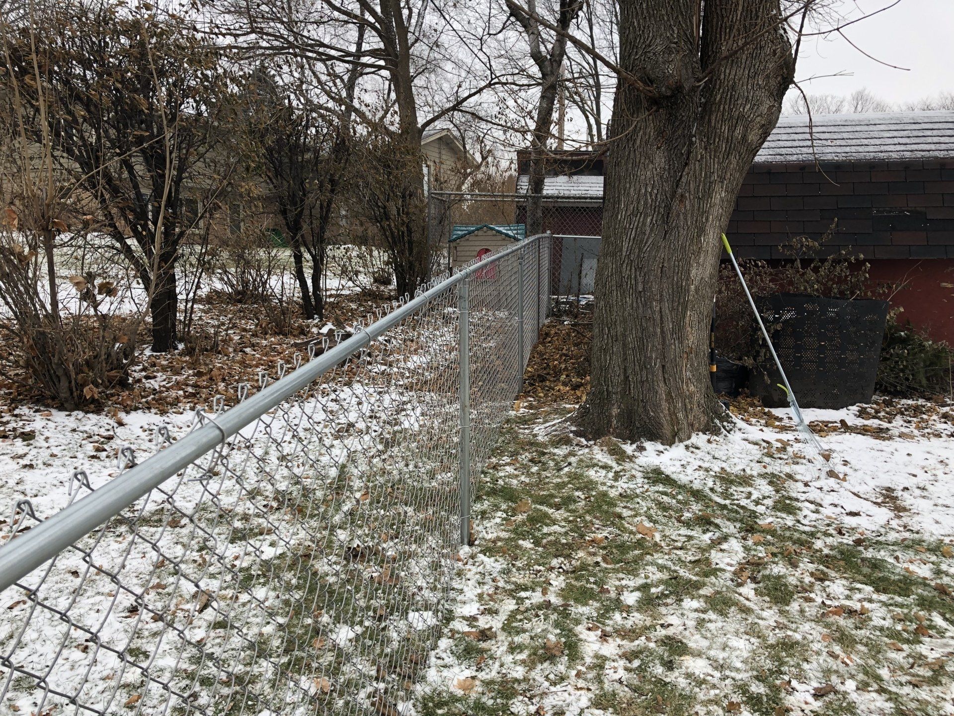 A chain link fence is surrounded by snow and trees.