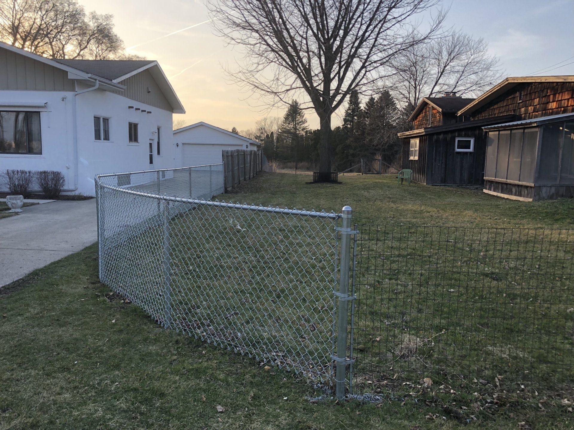 A chain link fence surrounds a lush green yard in front of a house.