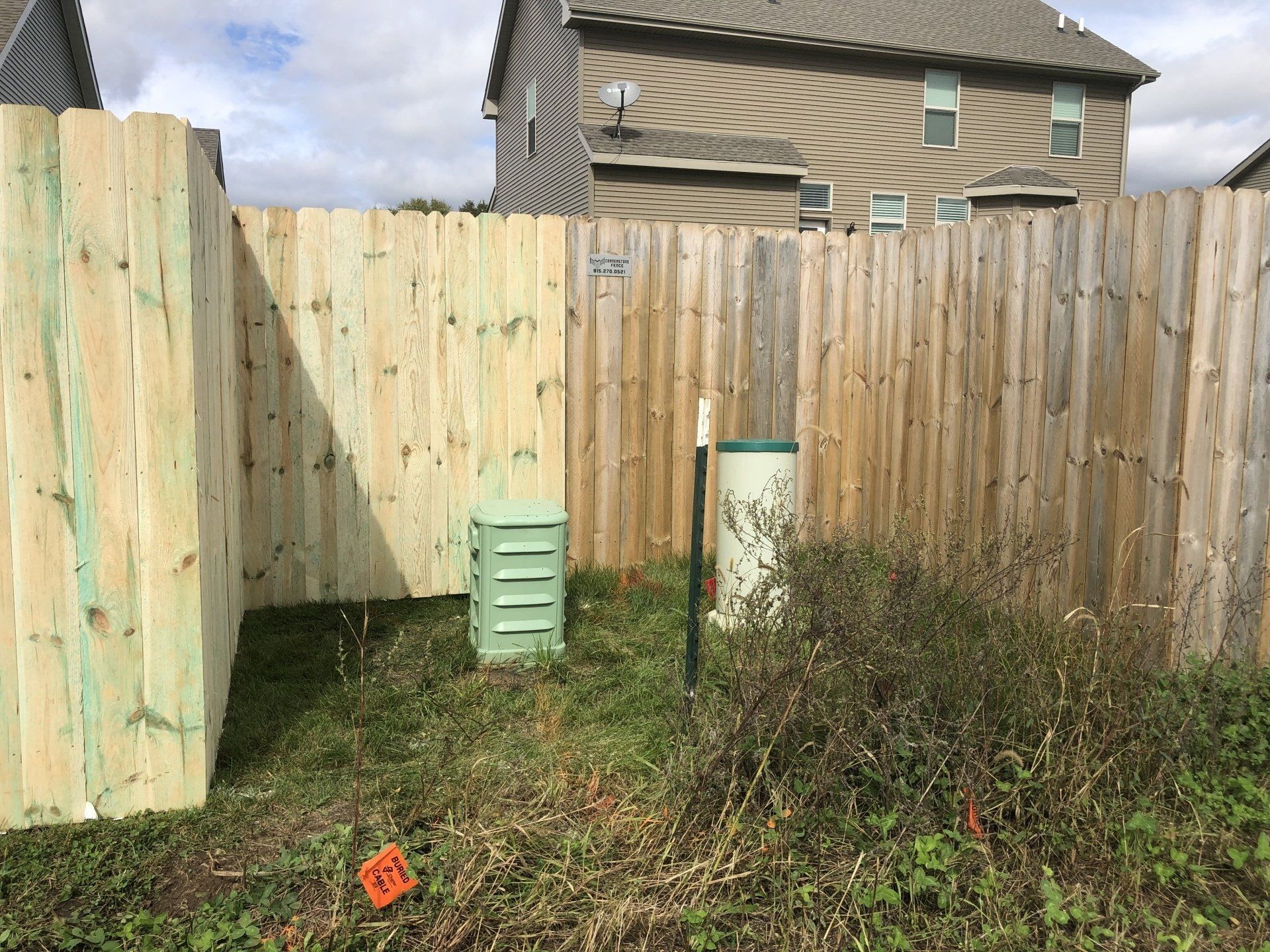 A wooden fence surrounds a grassy area in front of a house