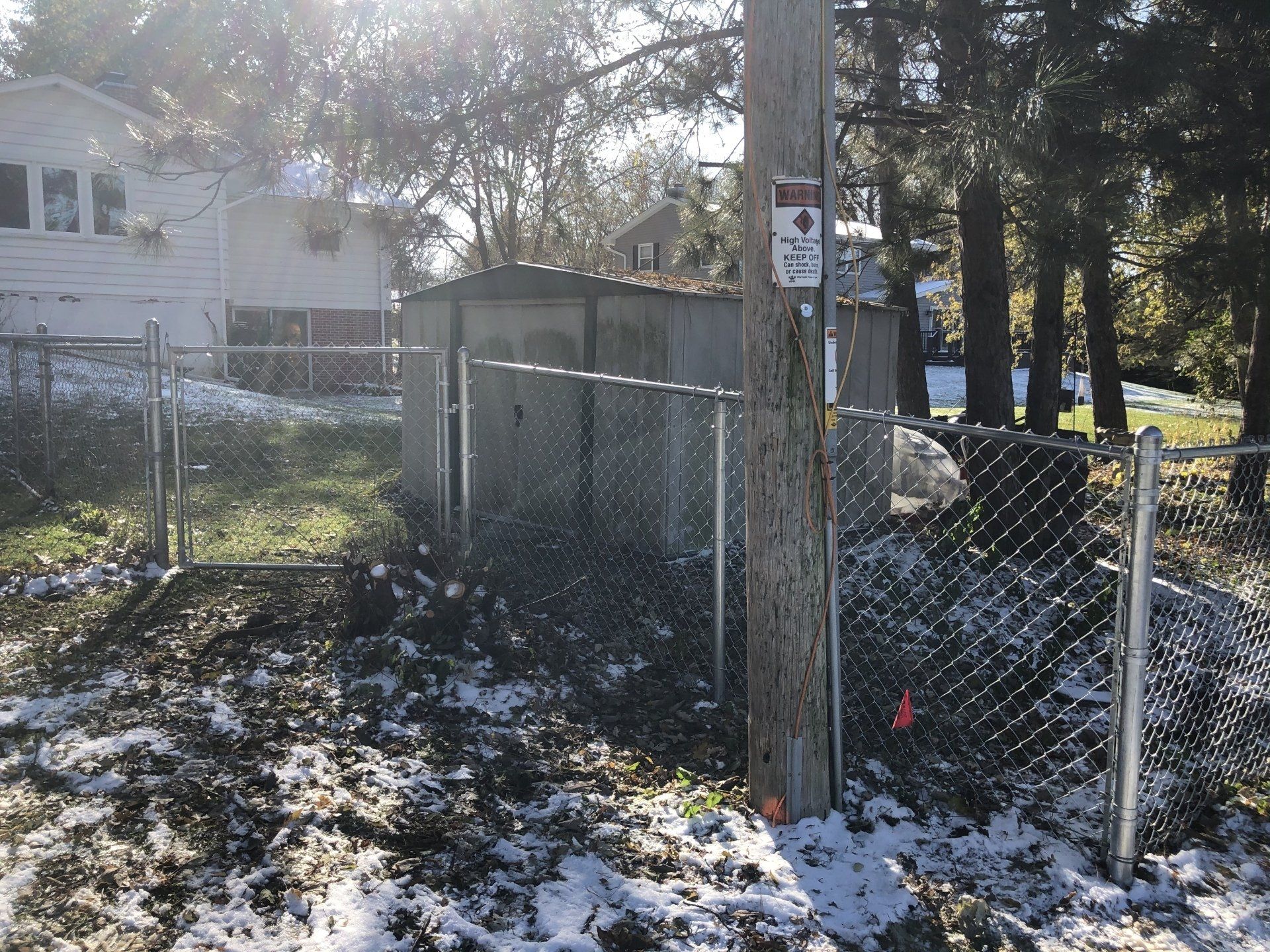 A chain link fence is surrounded by snow and trees