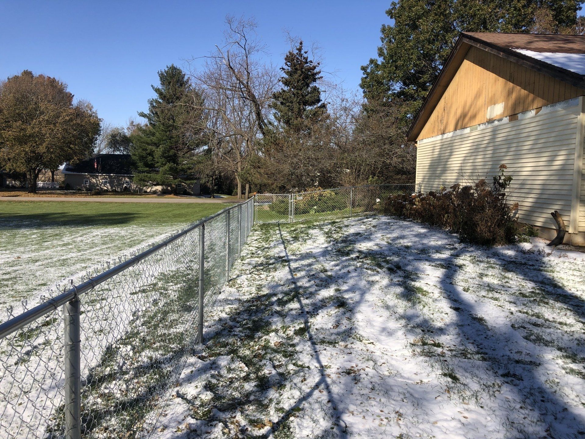 A snowy yard with a chain link fence and a house in the background.