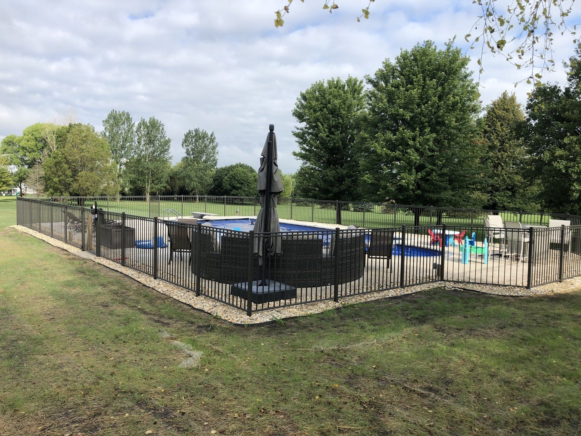 A fence surrounds a large swimming pool in a backyard.