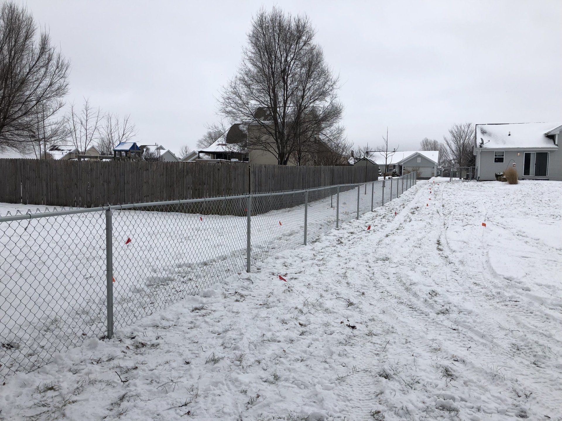 A chain link fence is surrounded by snow and a dirt road.