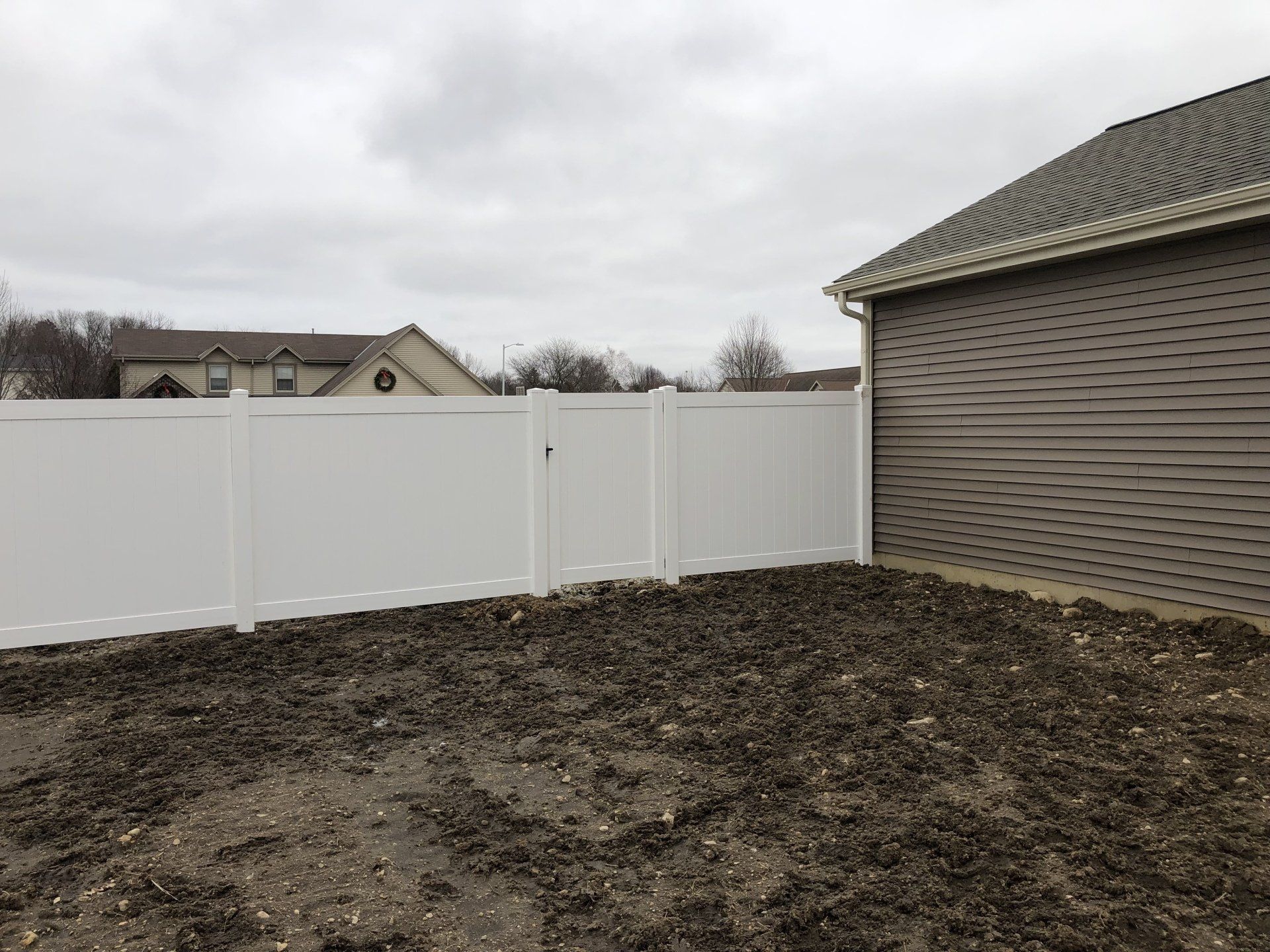 A white fence surrounds a dirt yard in front of a house.