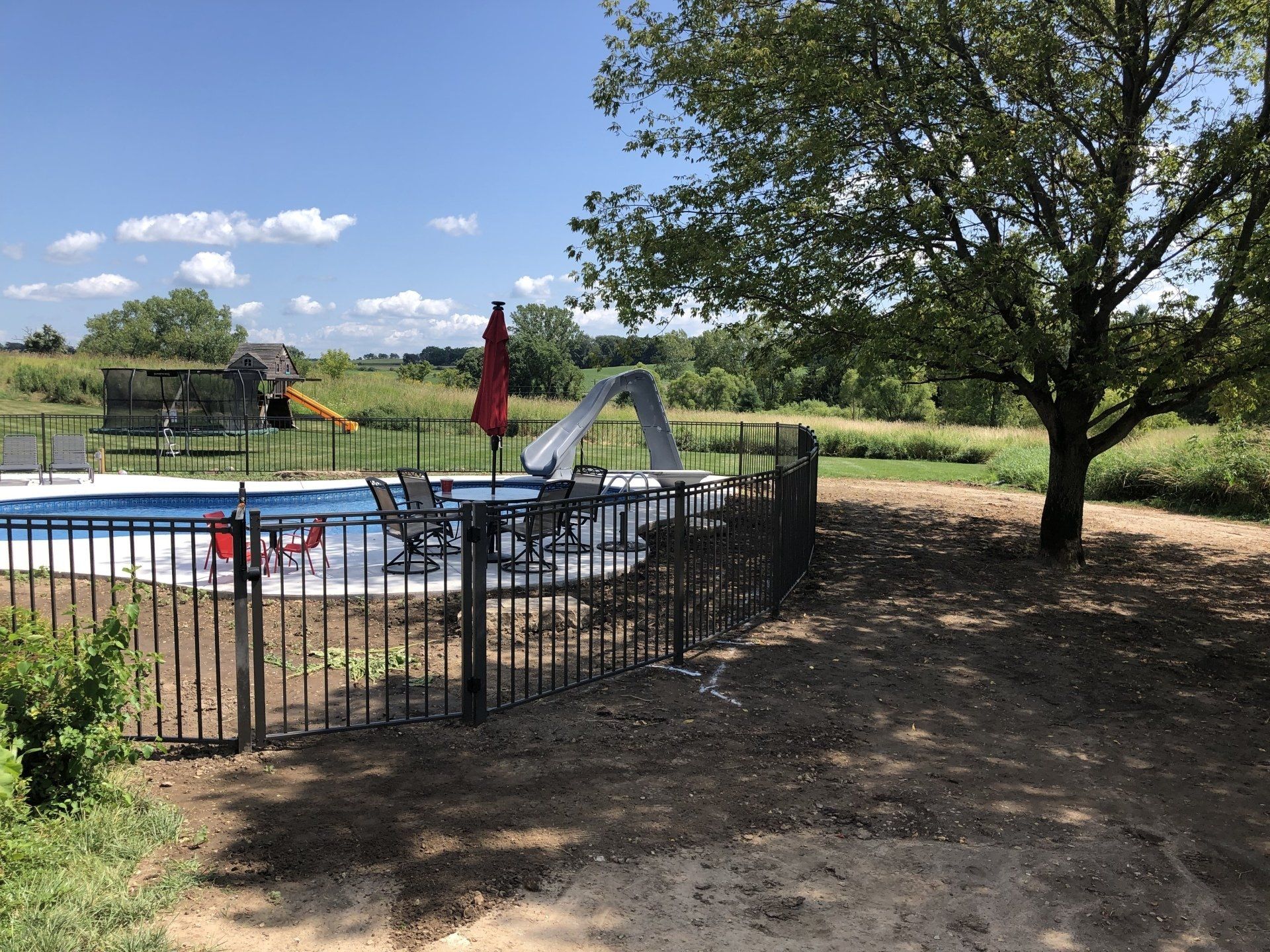 A fence surrounds a swimming pool with a slide and umbrella.