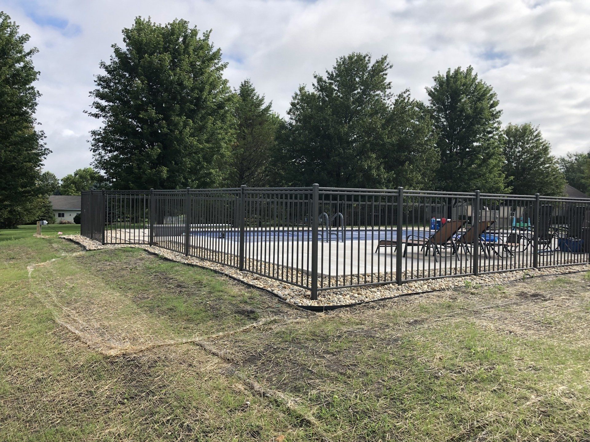 A fence around a swimming pool with chairs and trees in the background
