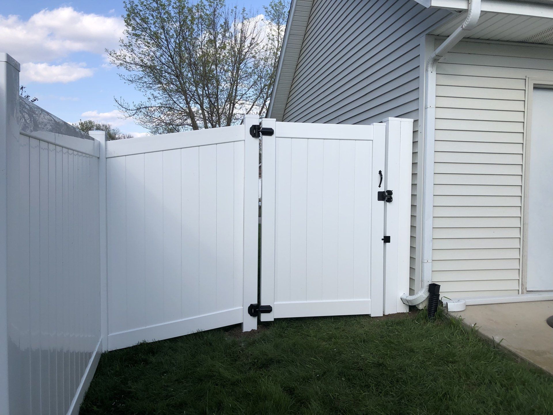 A white fence with a black gate is in front of a house.