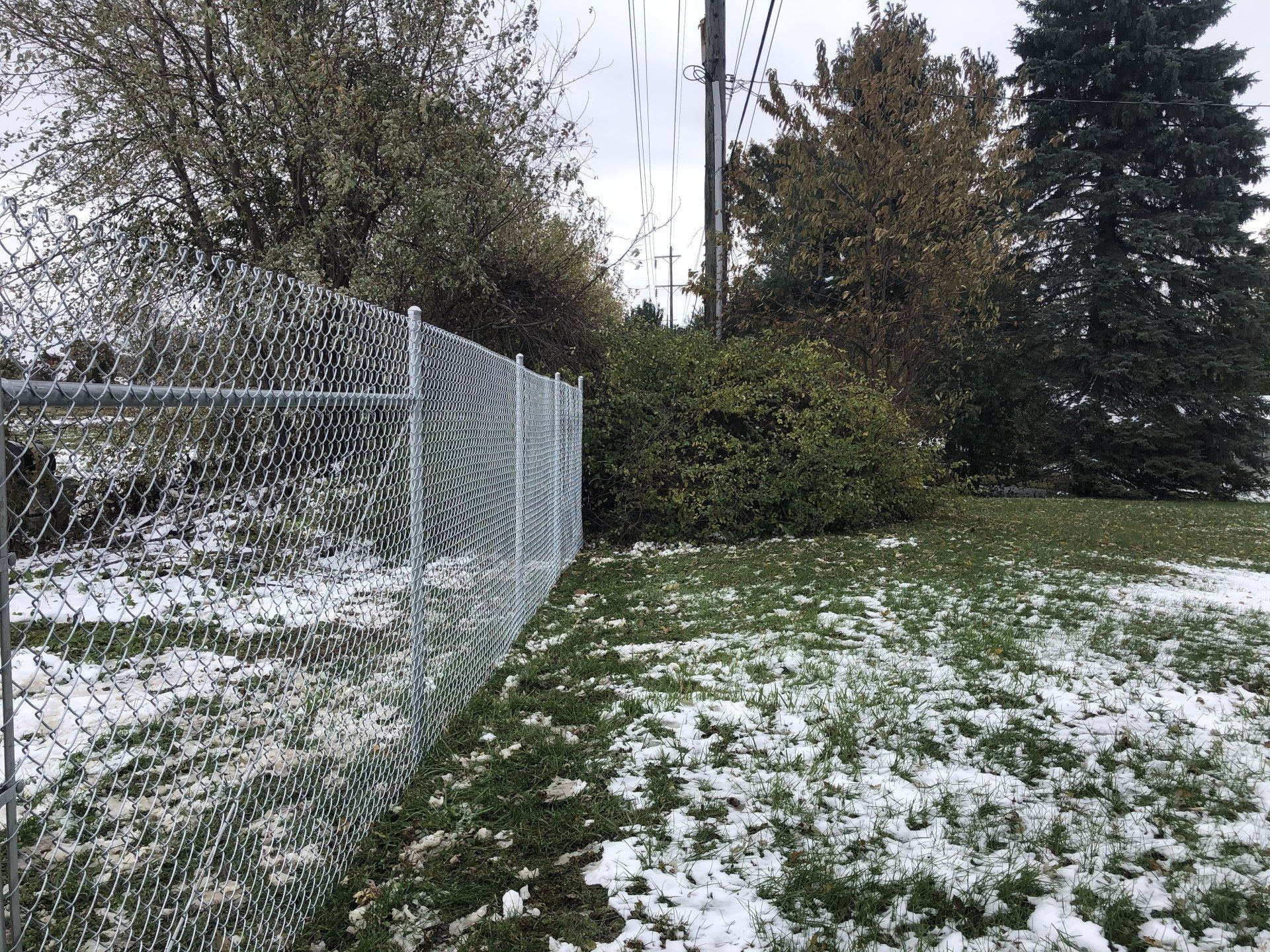 A chain link fence surrounds a grassy field with snow on the ground.