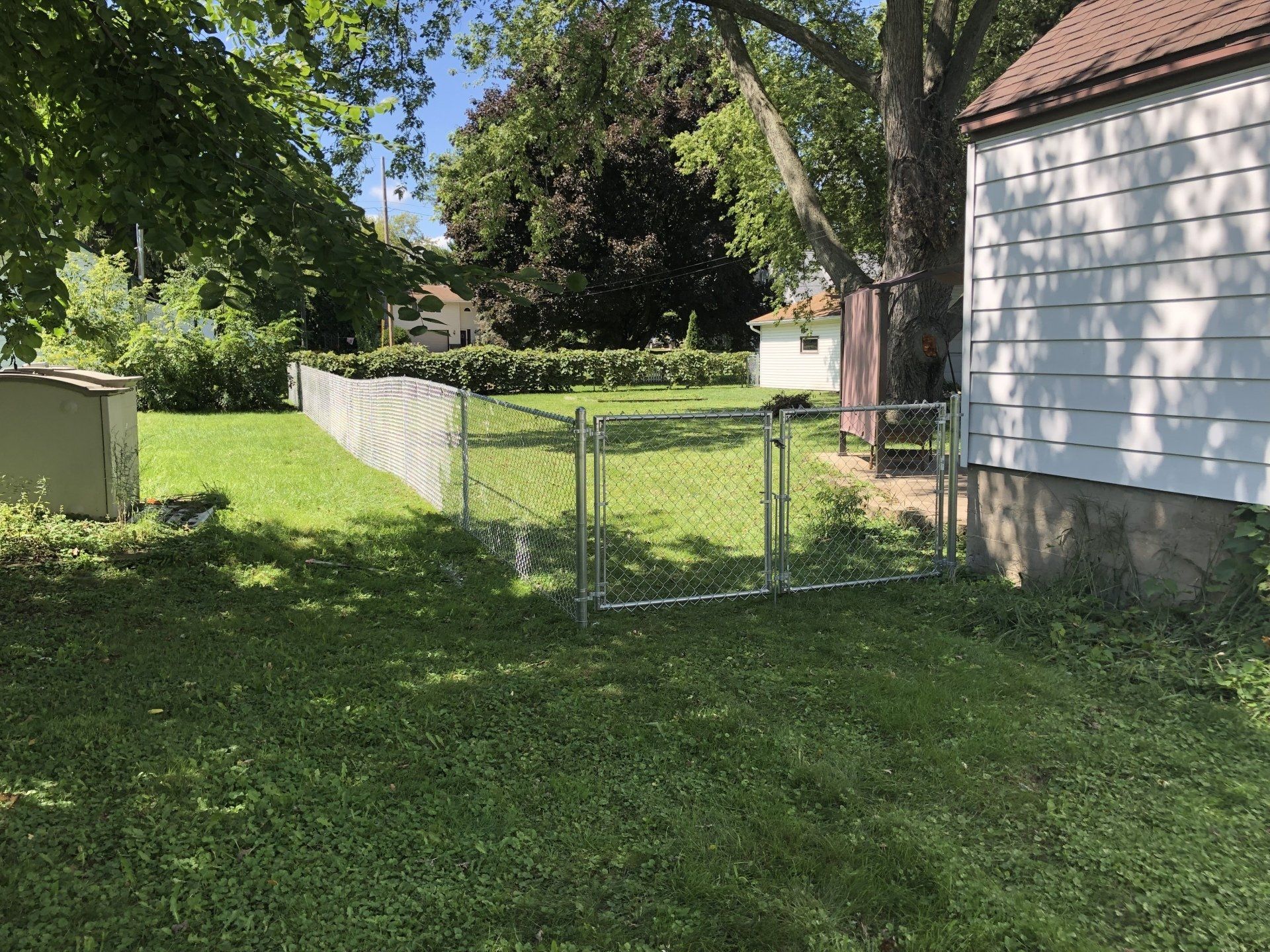 A backyard with a fence and a white house in the background.