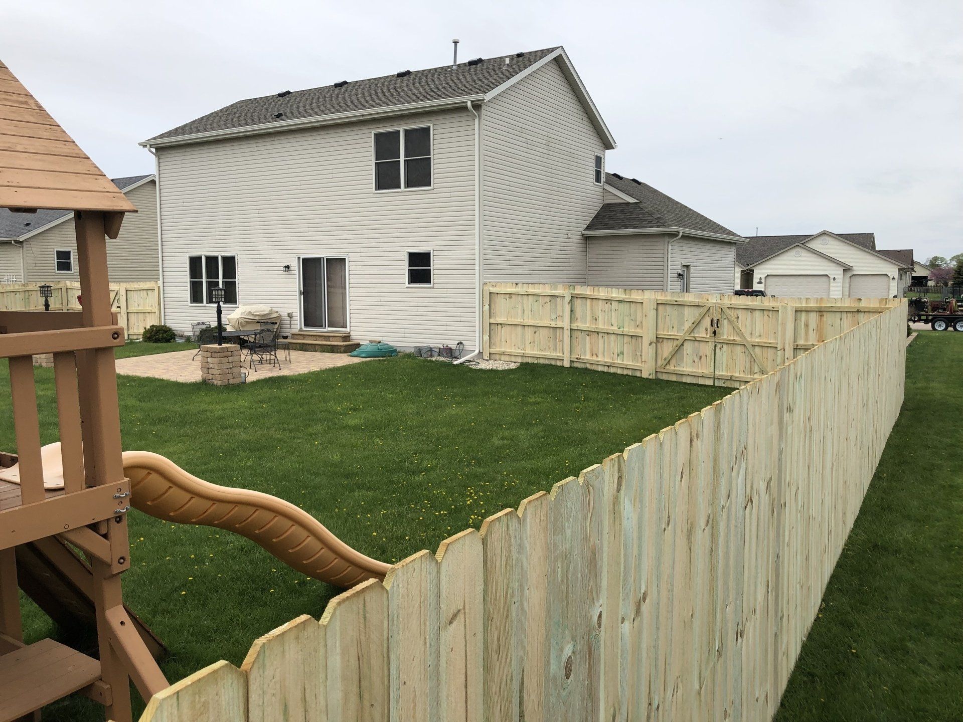A wooden fence surrounds a backyard with a house in the background.