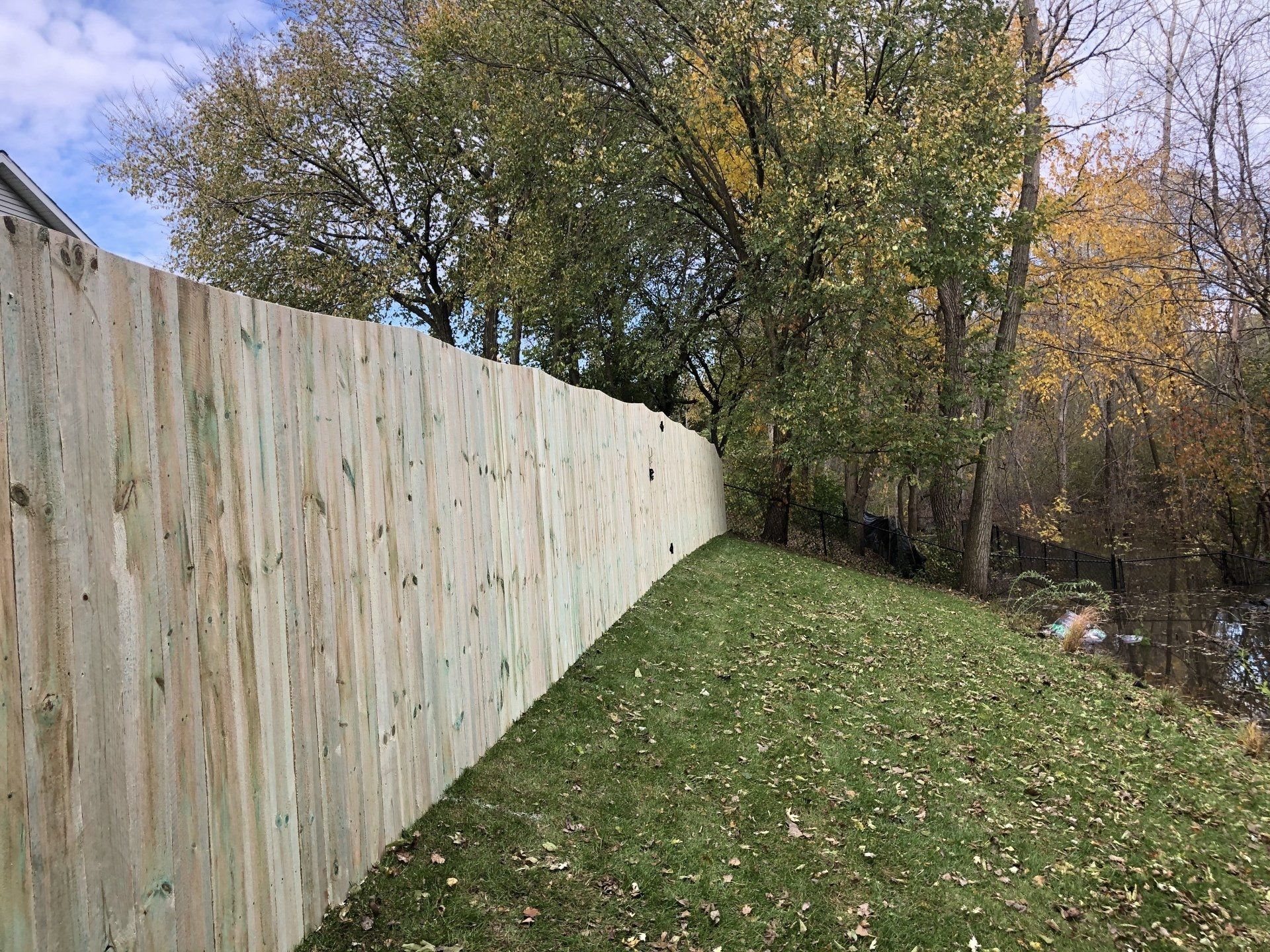 A wooden fence surrounds a lush green field with trees in the background.