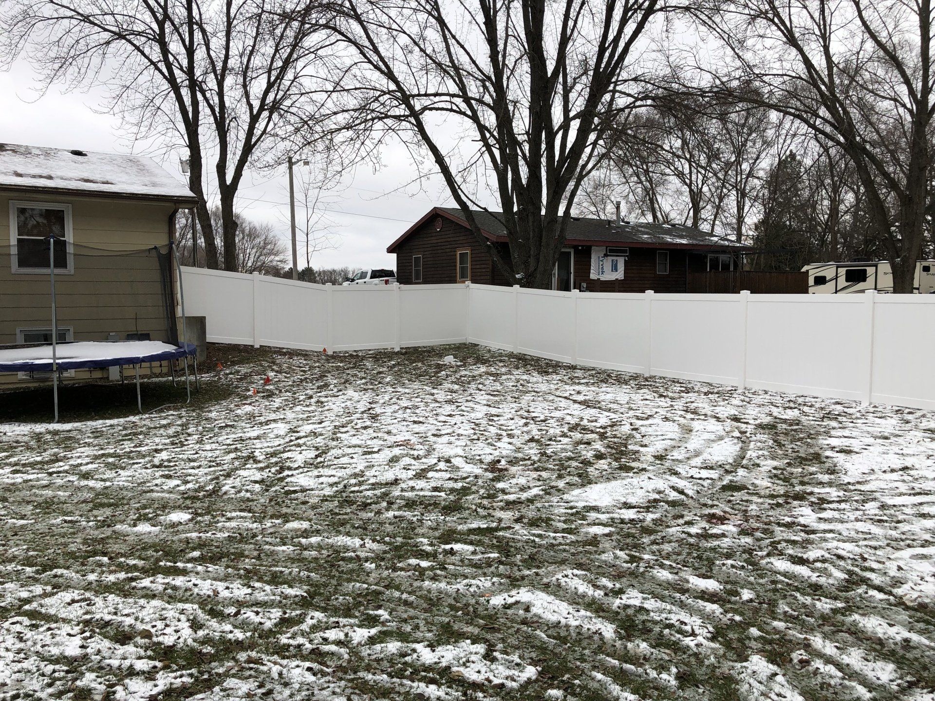 A white fence surrounds a snowy yard in front of a house.