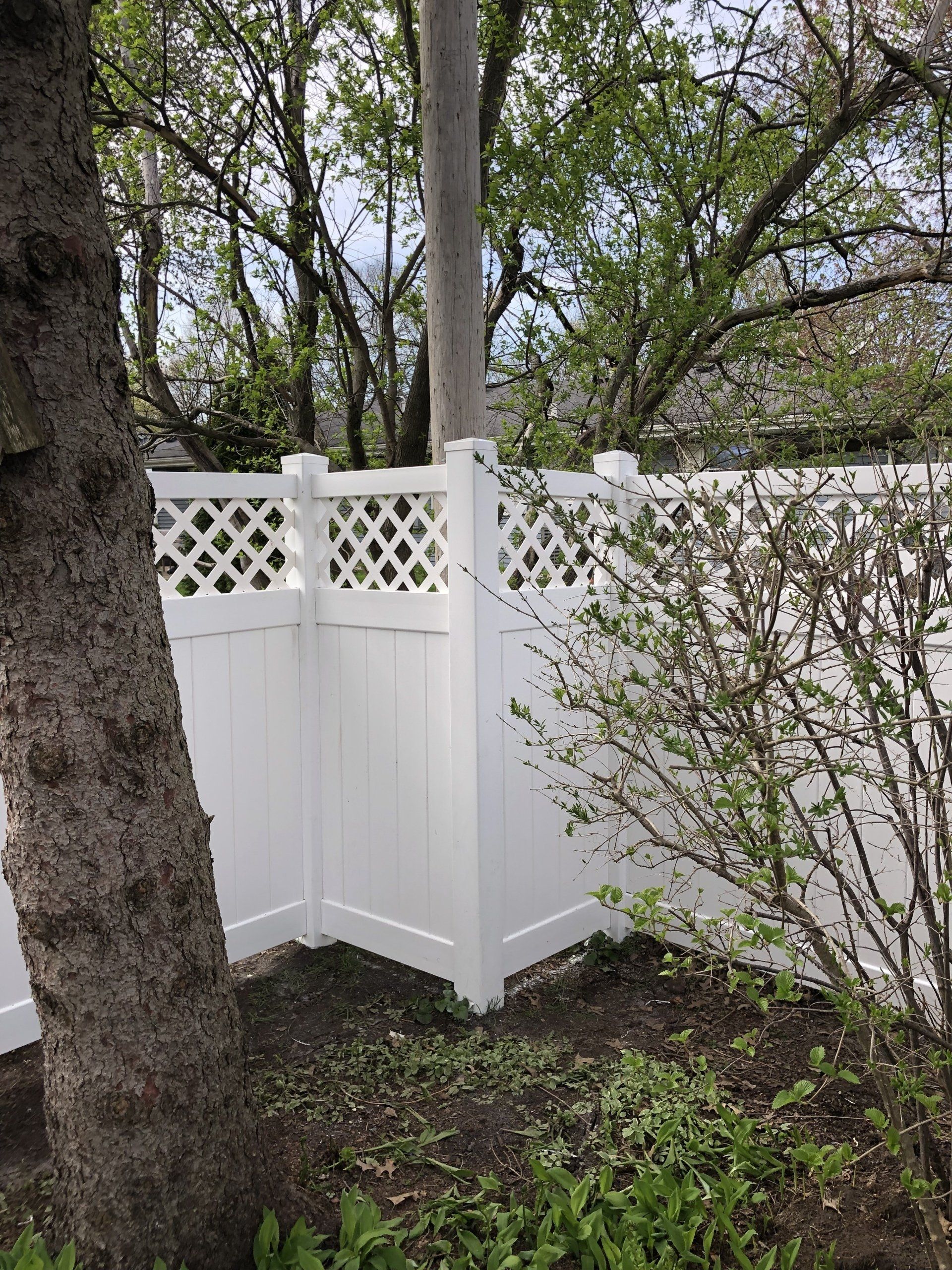 A white fence is surrounded by trees and bushes in a yard.